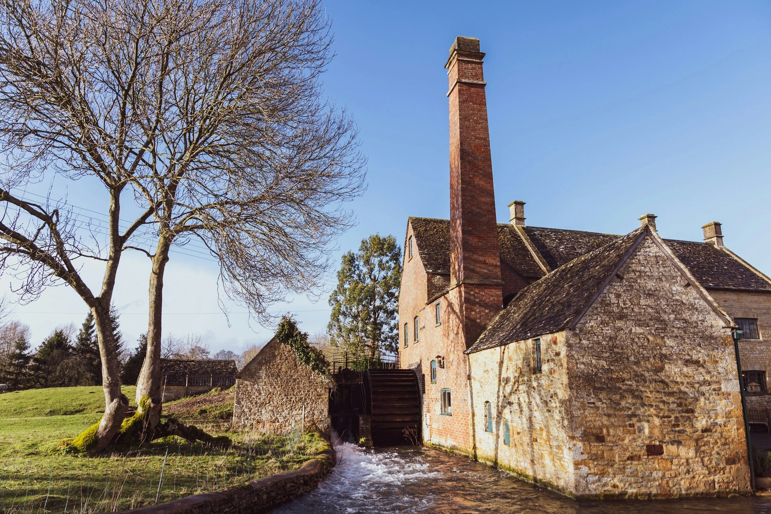 The Old Mill at Lower Slaughter, a honey-stone mill with a tall brick chimney and a water wheel on the stream