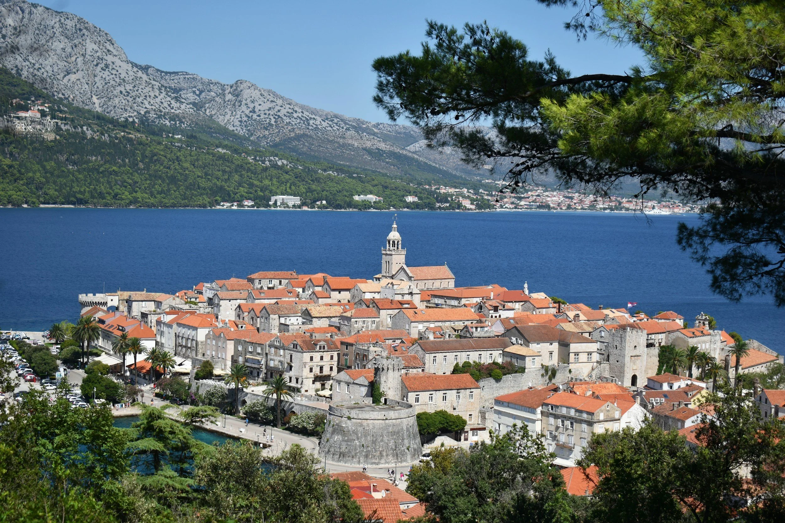 Korčula Old Town's red-roofed stone houses and cathedral tower on a small peninsula, with mountains across the blue channel