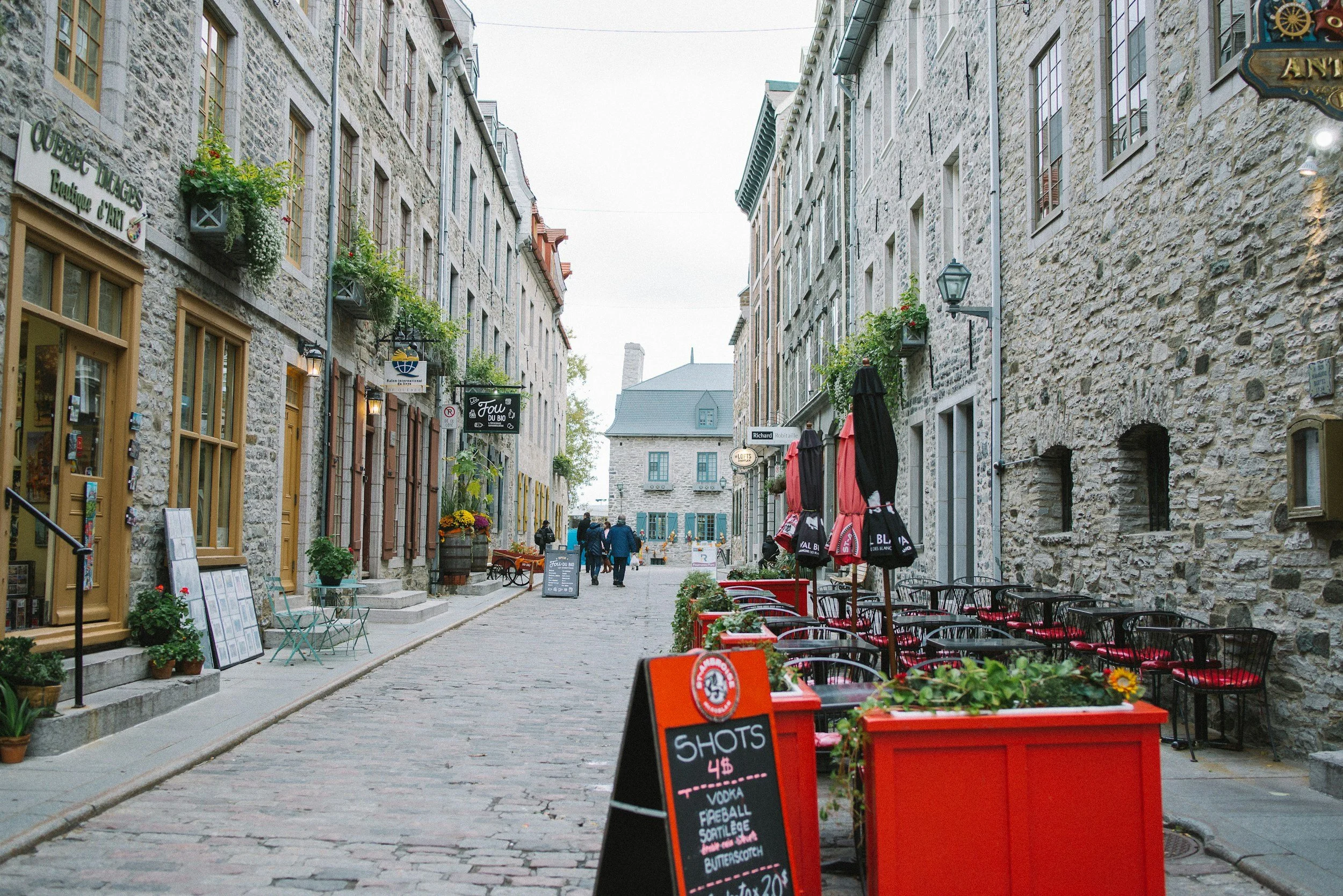 A narrow cobblestone street in Old Quebec lined with stone buildings, flower boxes and café tables
