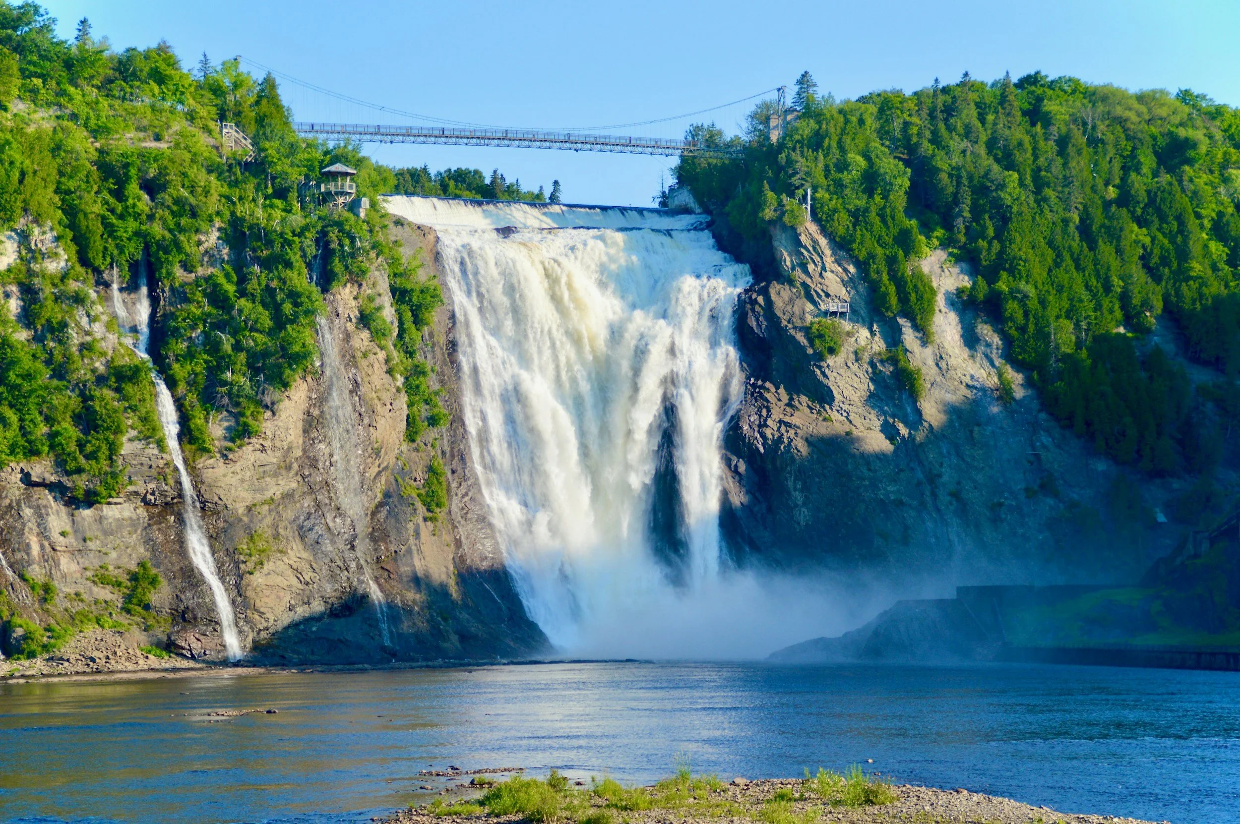 Montmorency Falls pouring down a rocky cliff between green trees, with a suspension bridge across the top