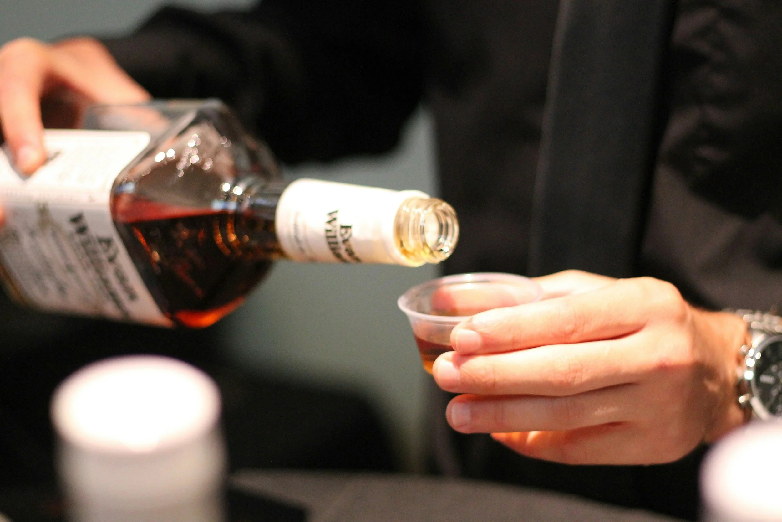 A pour of bourbon from a bottle into a small tasting cup