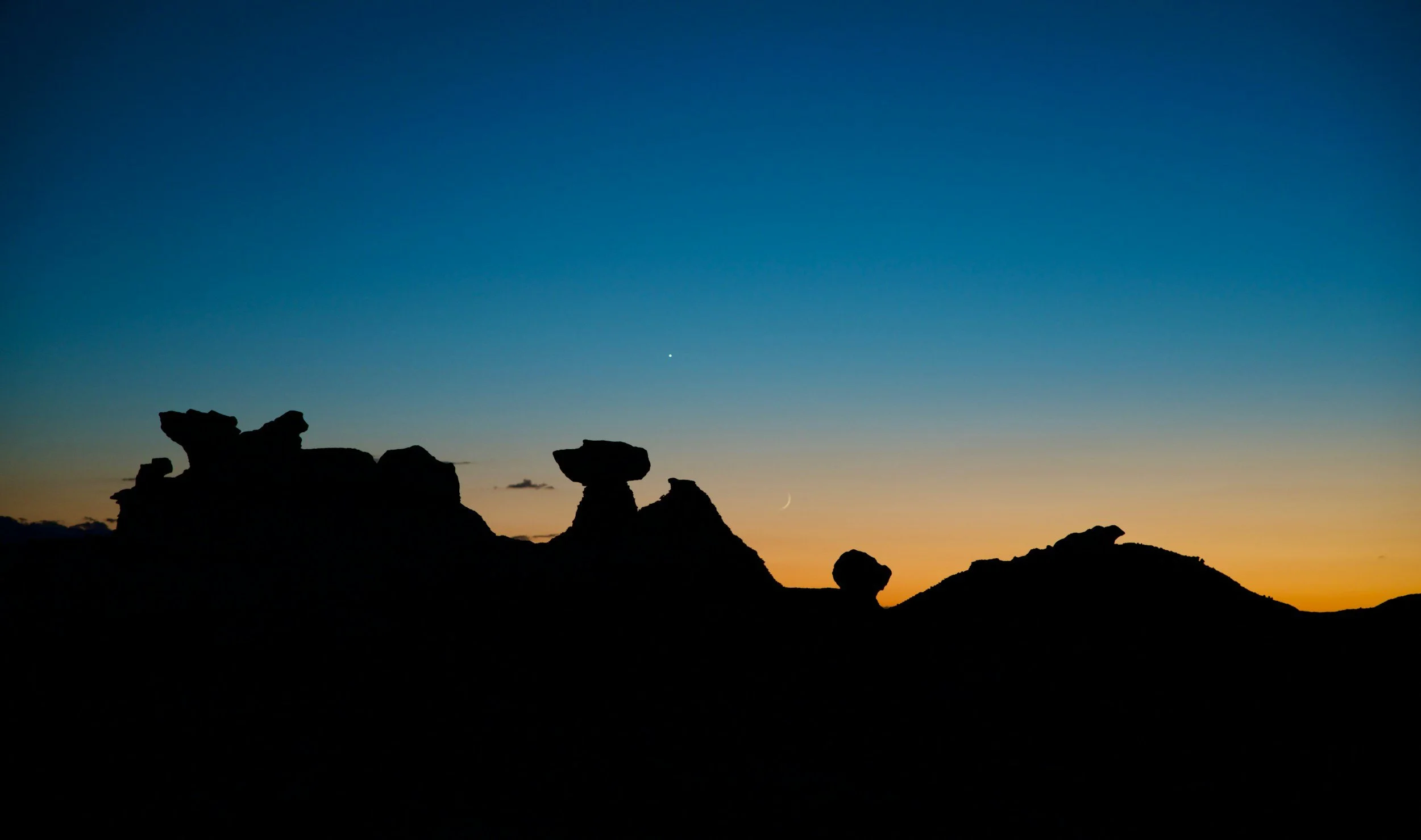 Mushroom-shaped hoodoo rock formations silhouetted against a blue and orange twilight sky