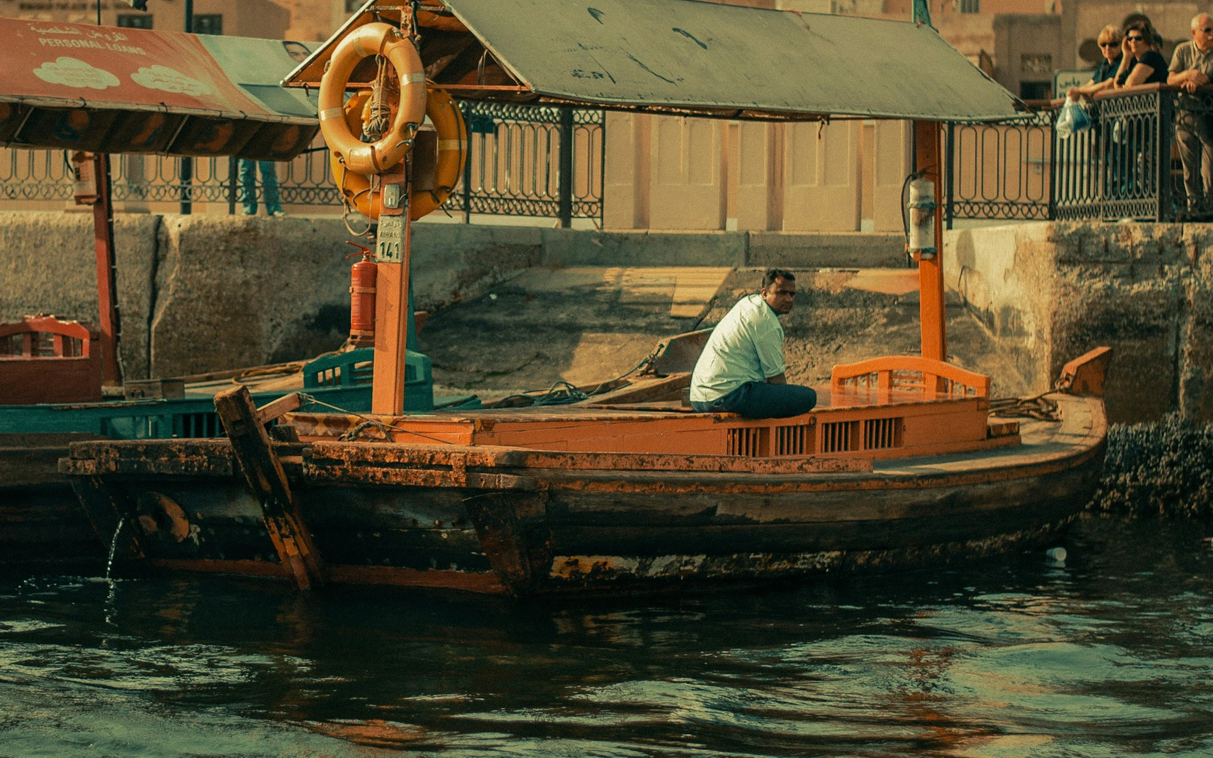 A traditional wooden abra boat moored on Dubai Creek, with a boatman sitting on board