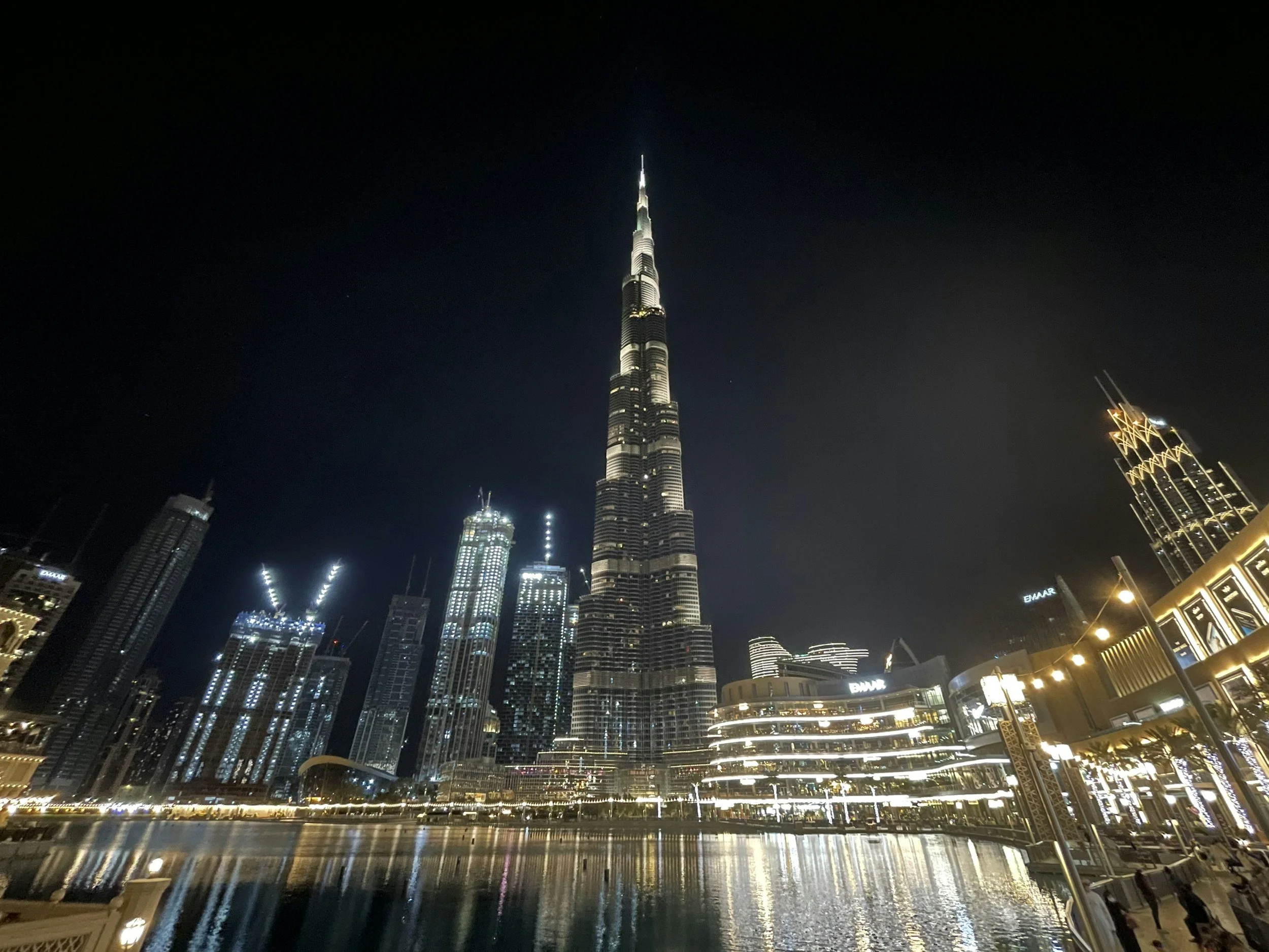 The Burj Khalifa lit up at night above downtown Dubai, with city lights reflected in the water