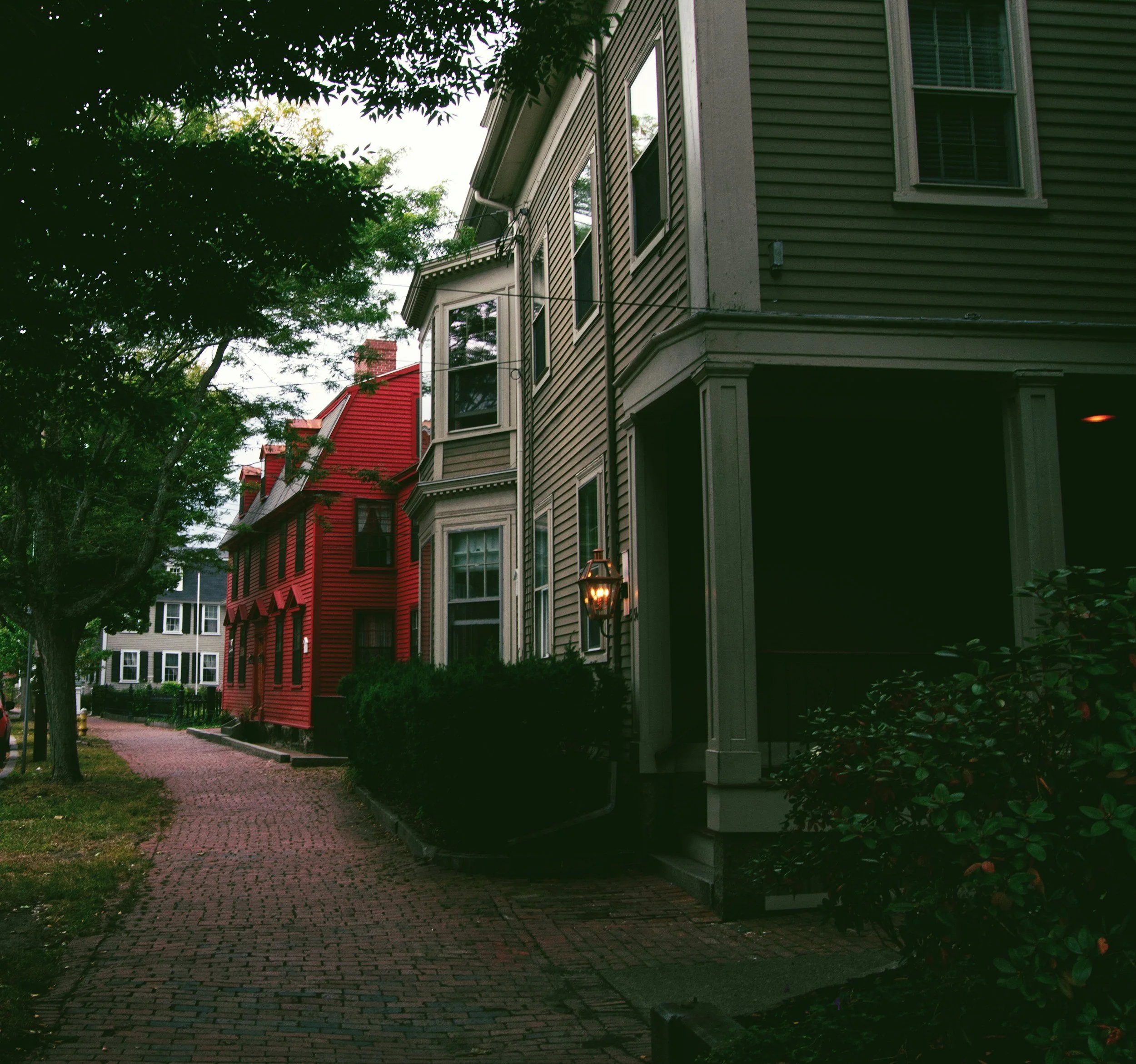 Quiet brick sidewalk lined with historic clapboard houses, one painted red