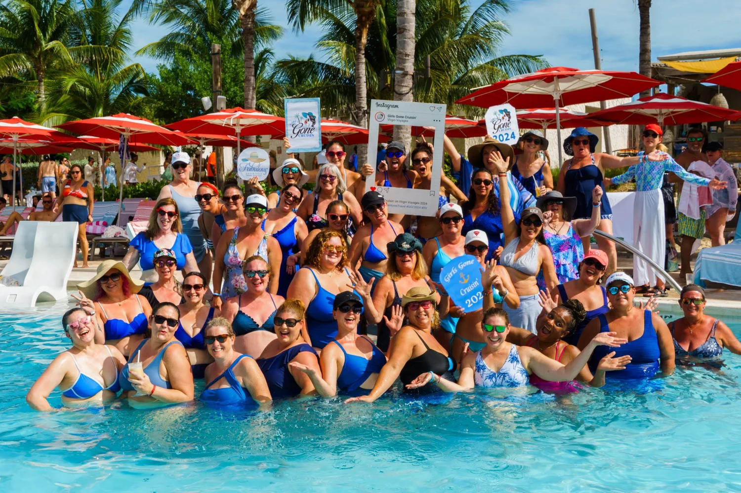 A big group of Girls Gone Cruisin' women posing together in a pool lined with red umbrellas