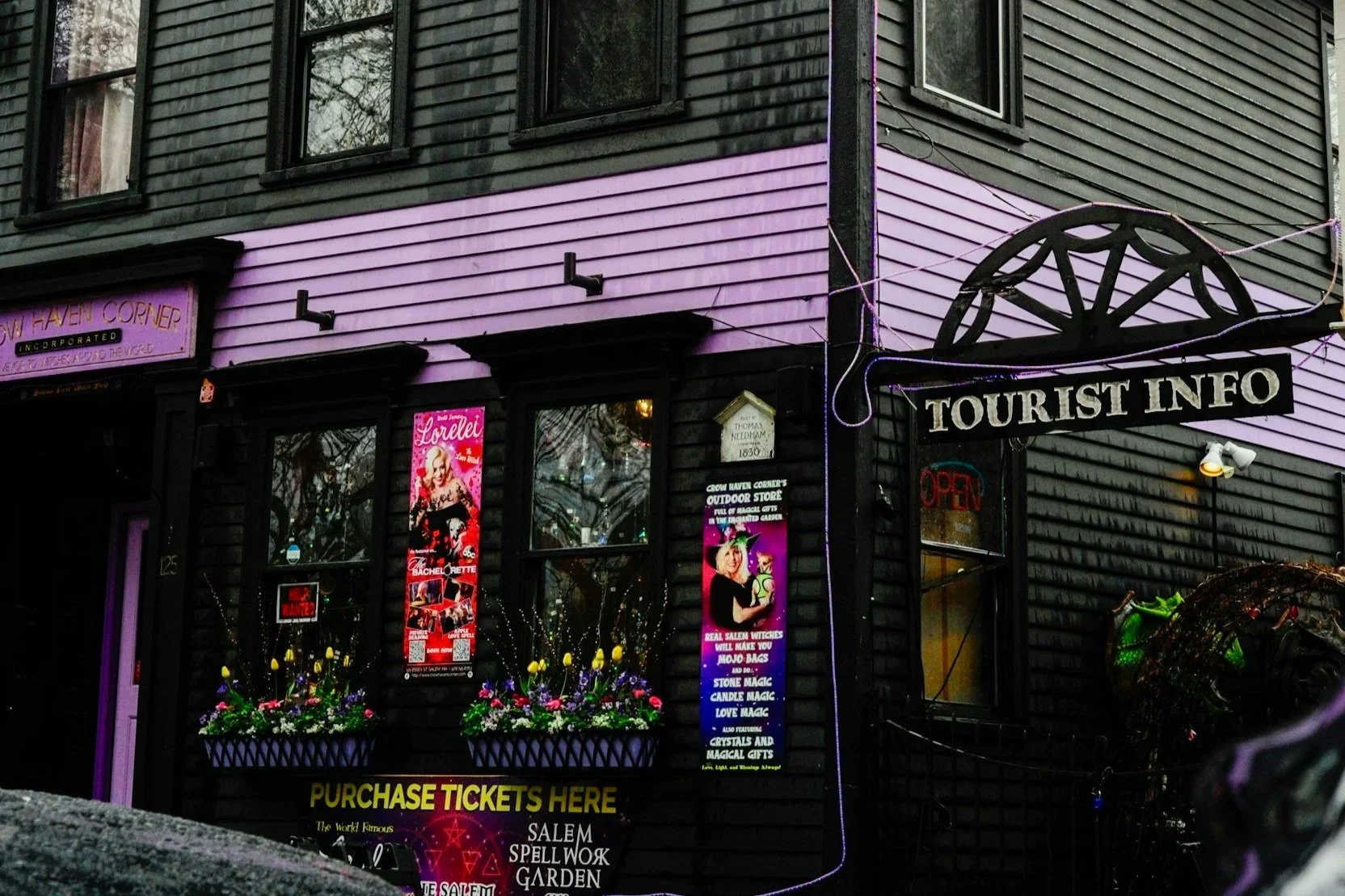 Witchy shopfront with purple trim, bright posters and window flower boxes under a Tourist Info sign in Salem