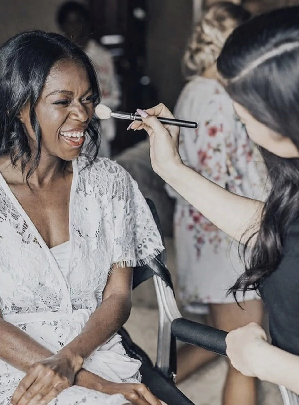 Makeup artist applying powder with a brush to a laughing woman’s face