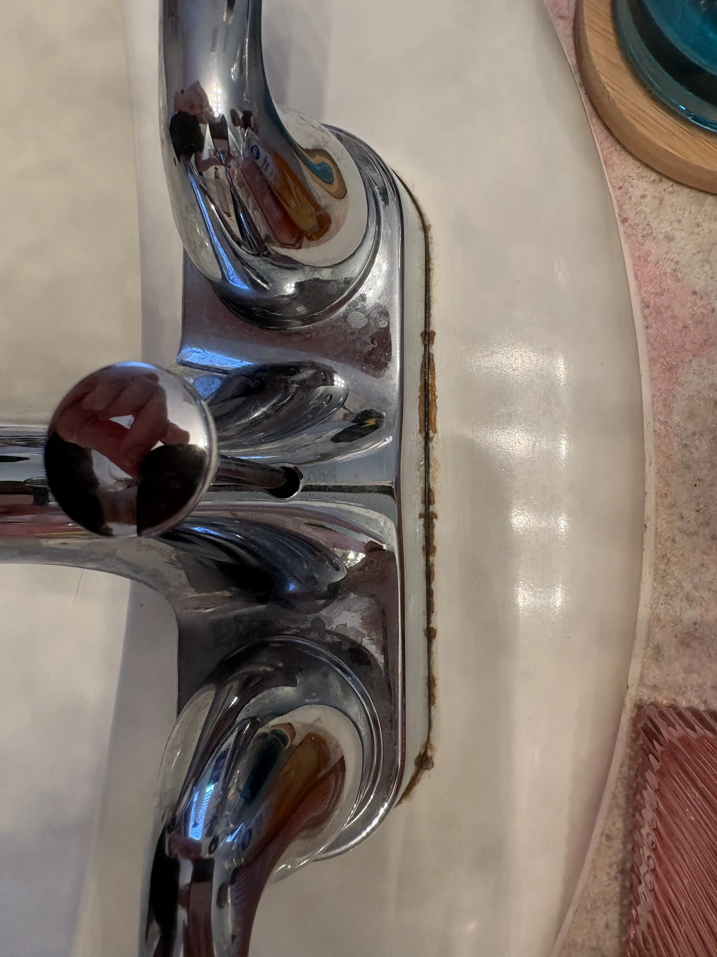 Close-up of a chrome bathroom faucet and handles mounted on a white sink, with a blue bowl and pink countertop visible.