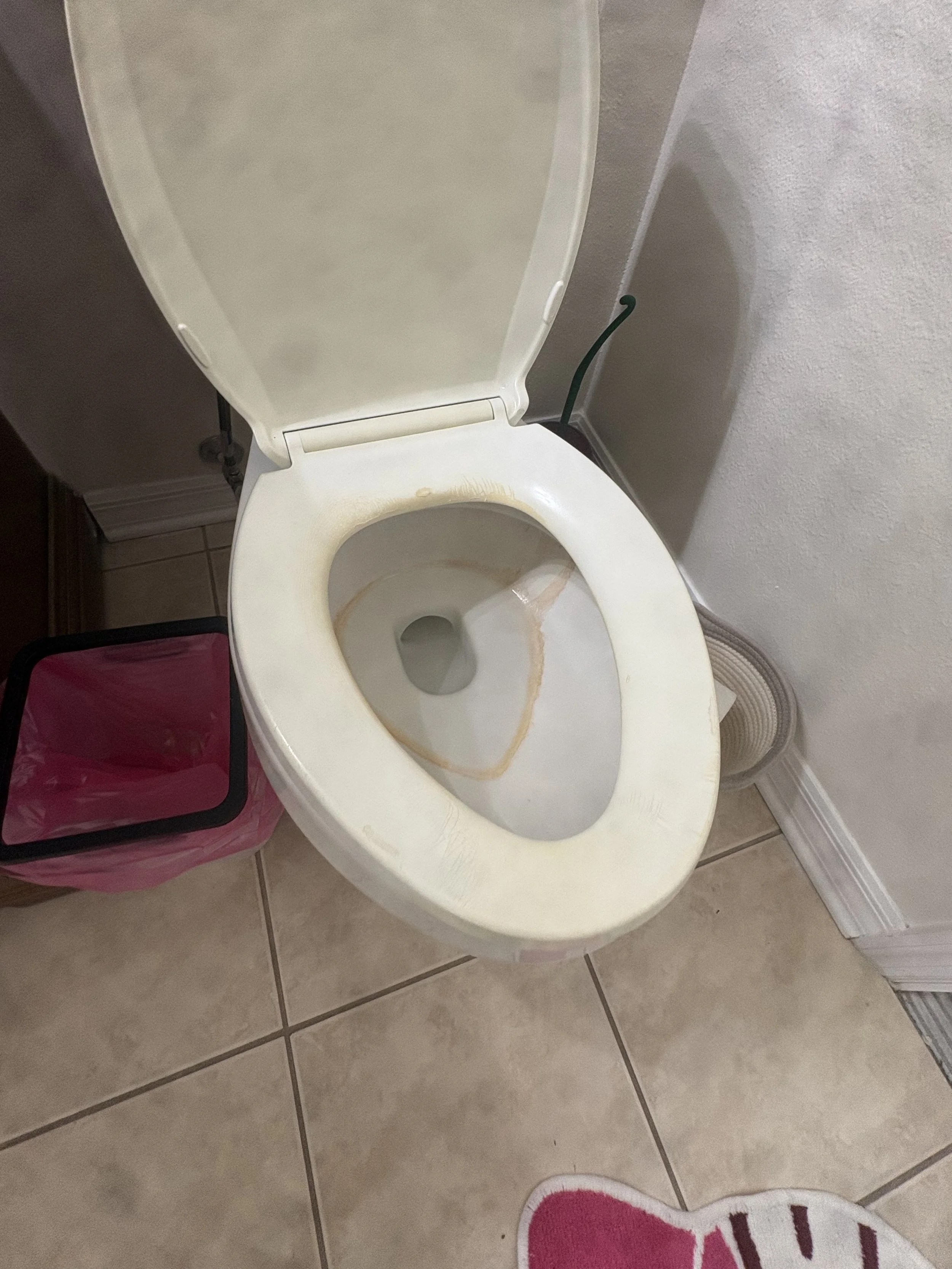 Open white toilet with stained bowl and raised lid in a tiled bathroom