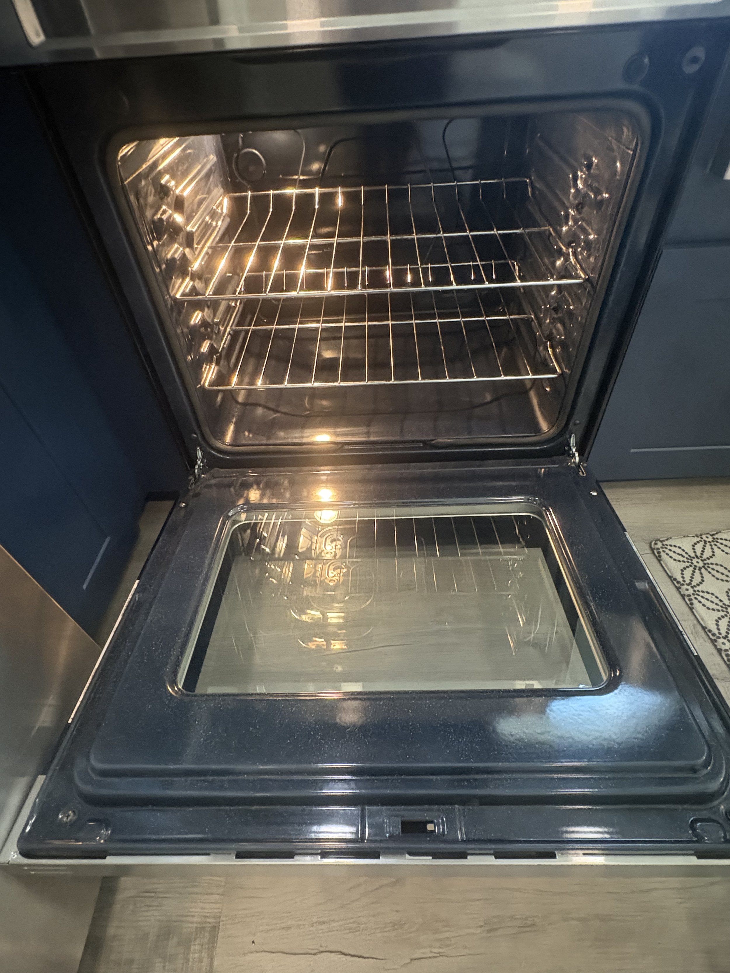 Open, empty electric oven with illuminated interior and multiple wire racks.