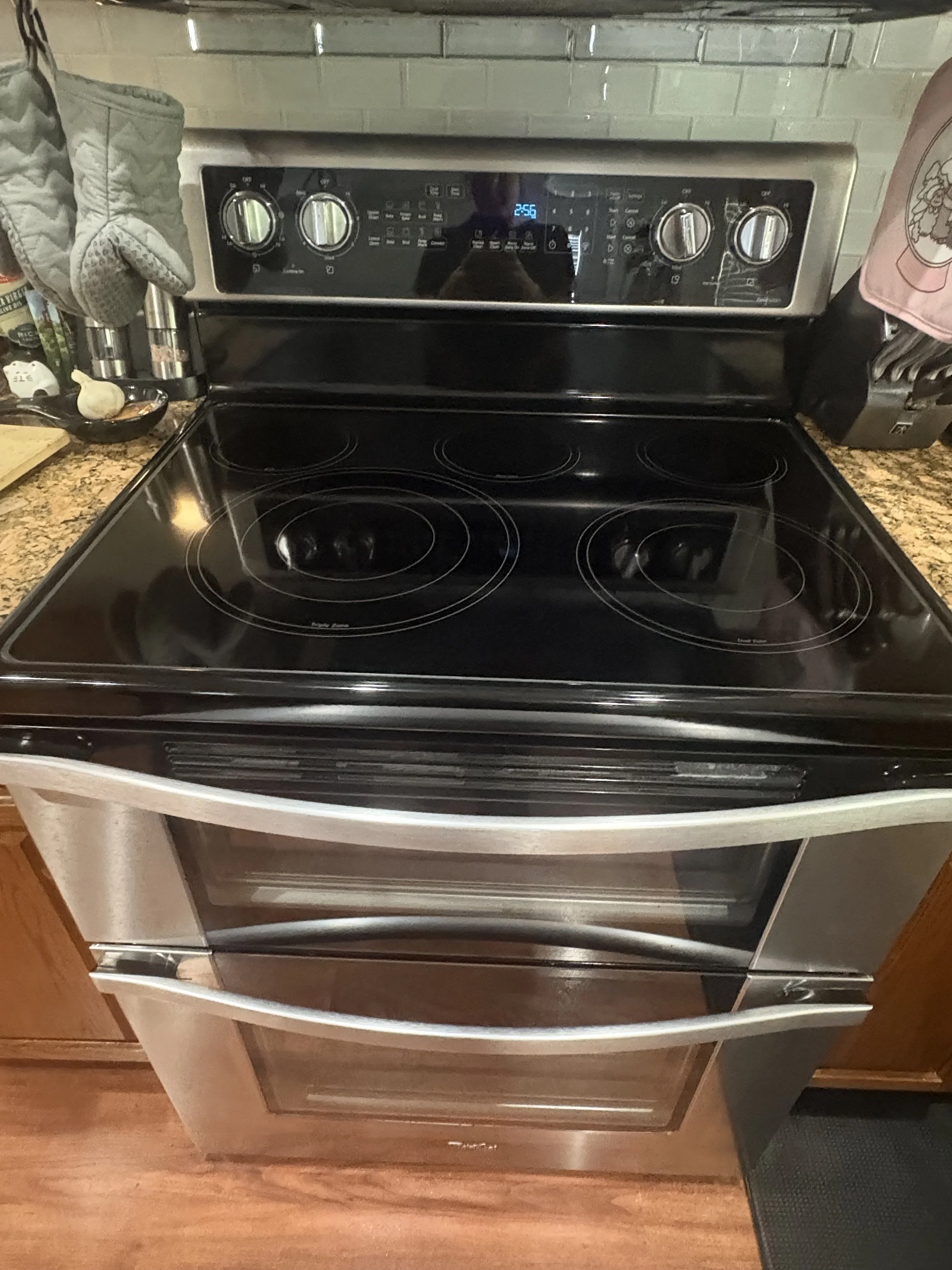 Black electric range with four burners, digital controls, and an open lower oven drawer in a kitchen.