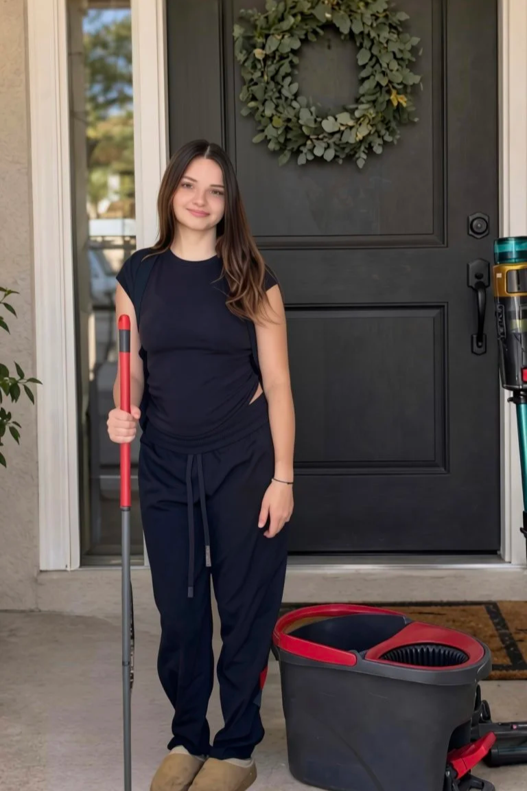 Woman holding a red-handled mop beside a spin mop bucket at a home's front door