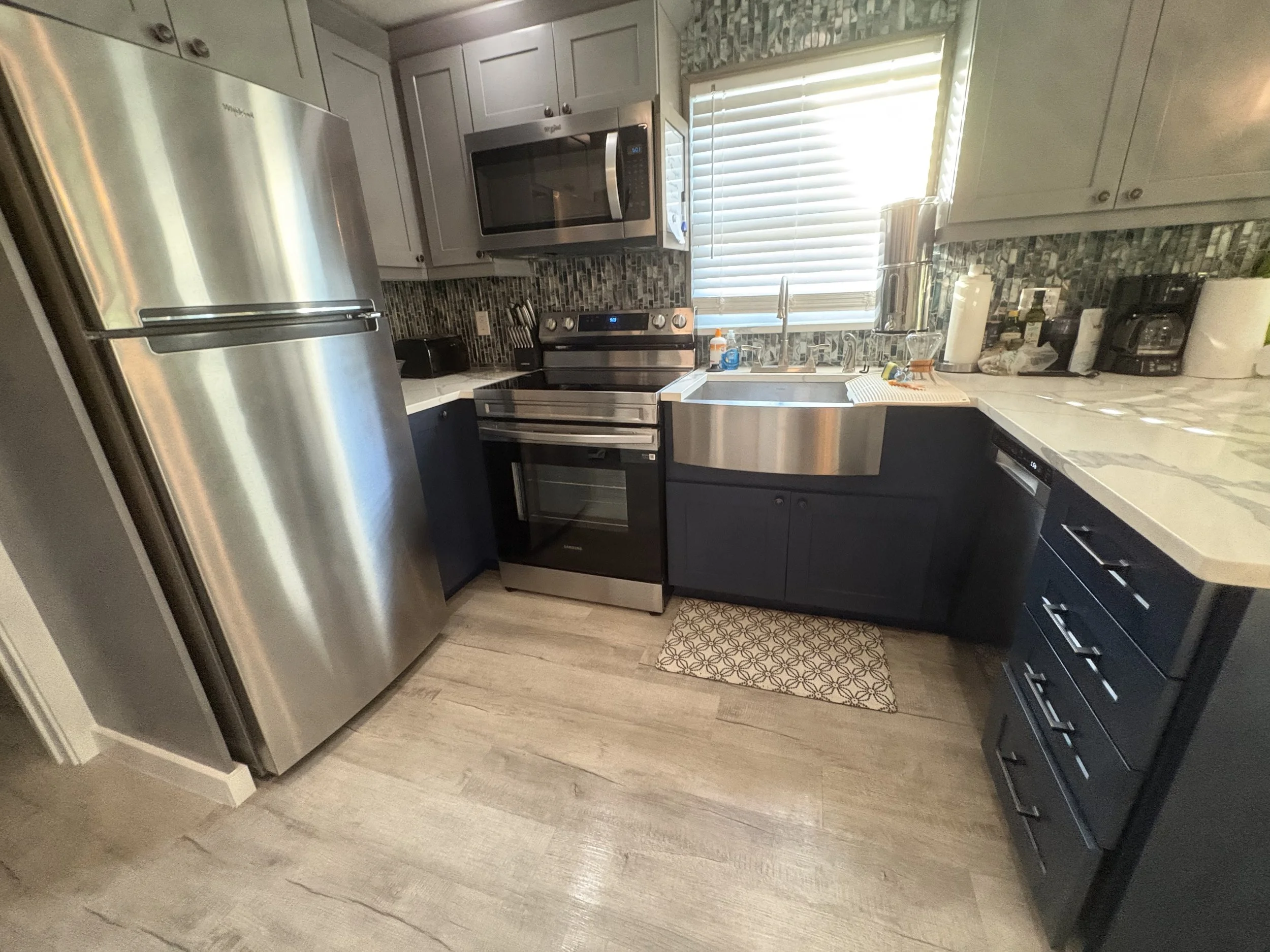 Modern compact kitchen with stainless steel refrigerator, electric range, microwave, sink, dark cabinets, mosaic backsplash, and white countertops