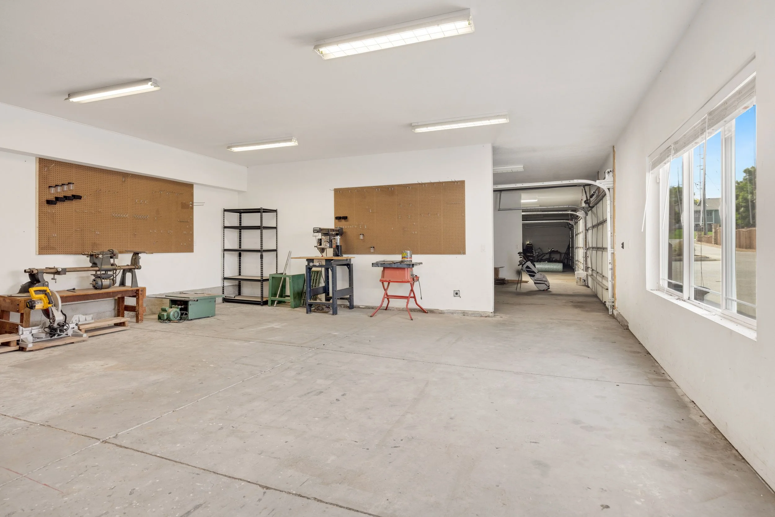 Spacious workshop garage with pegboards, woodworking tools, workbenches, shelving, fluorescent lights, and large windows