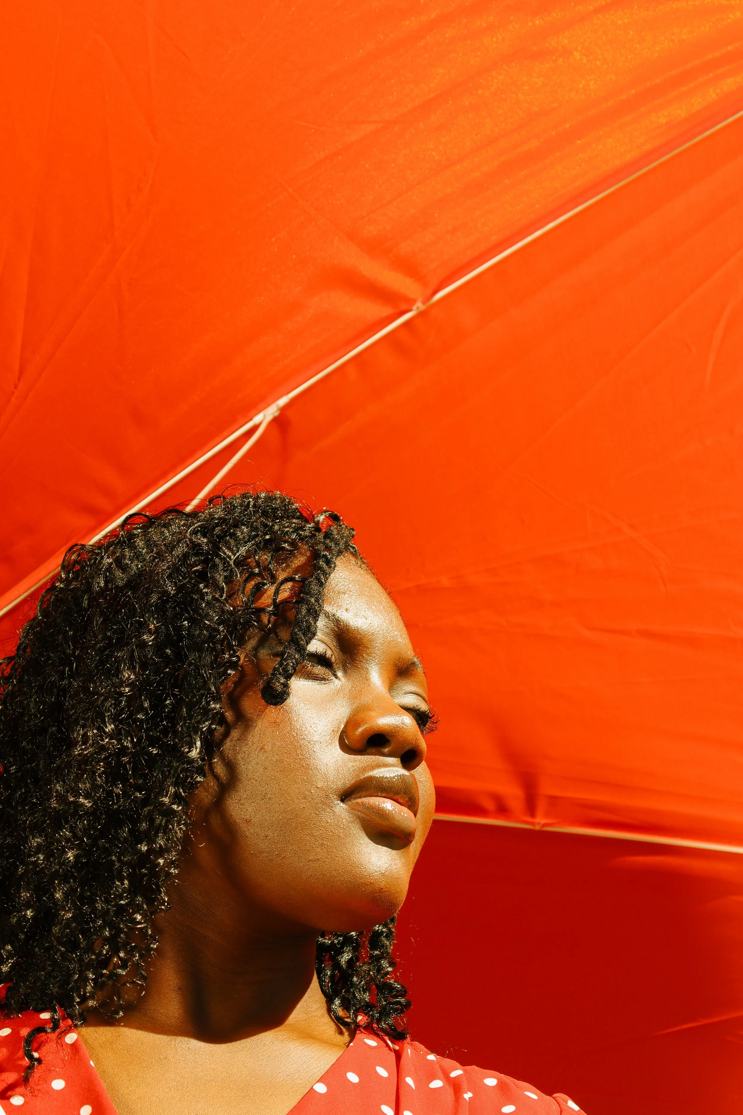 An editorial portrait photograph of Jane Simataa under a red umbrella looking to her right taken by Kim Kambinda in Windhoek, Namibia.