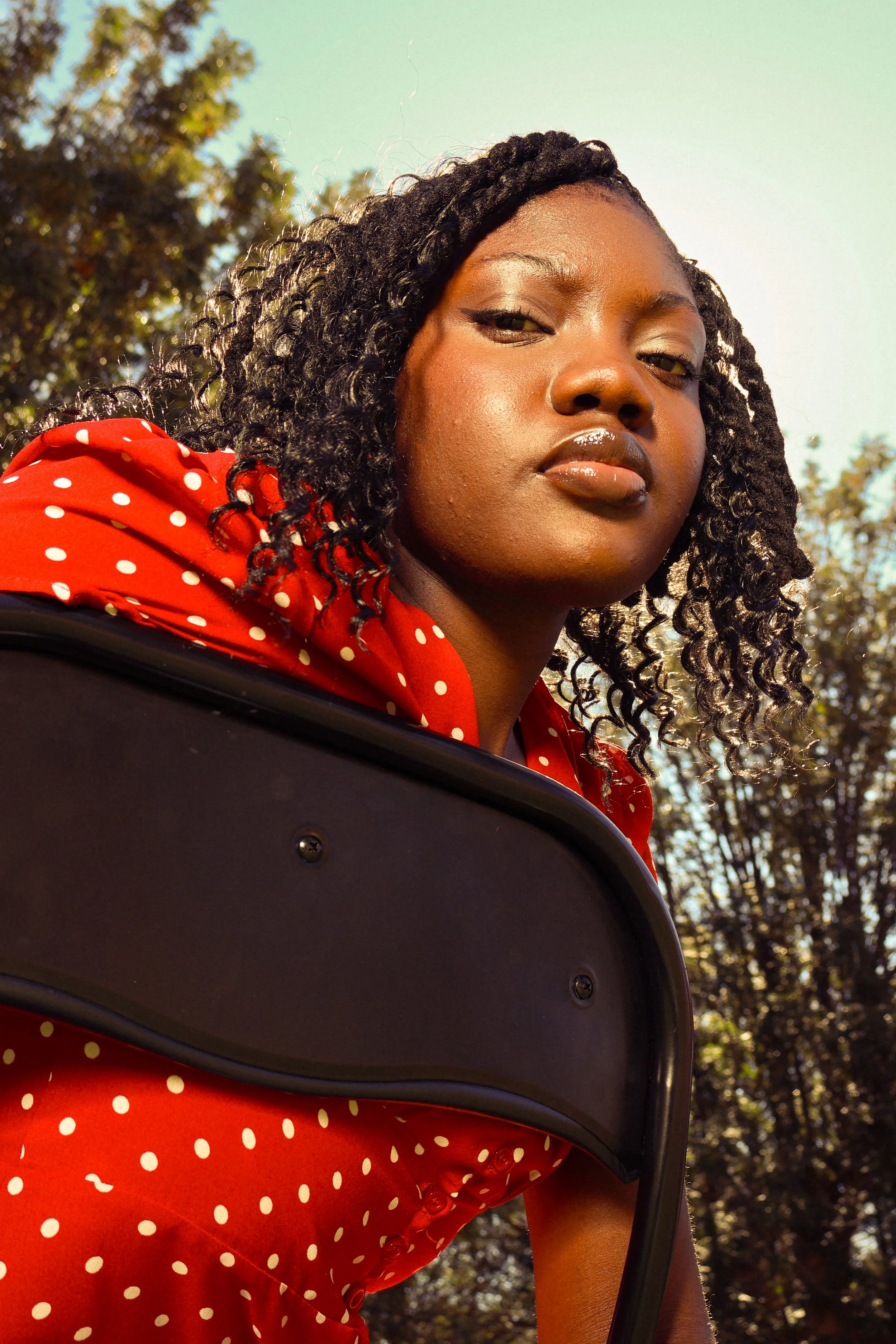 An editorial portrait photograph of Jane Simataa staring down at the camera while sitting on a chair taken by Kim Kambinda in Windhoek, Namibia.