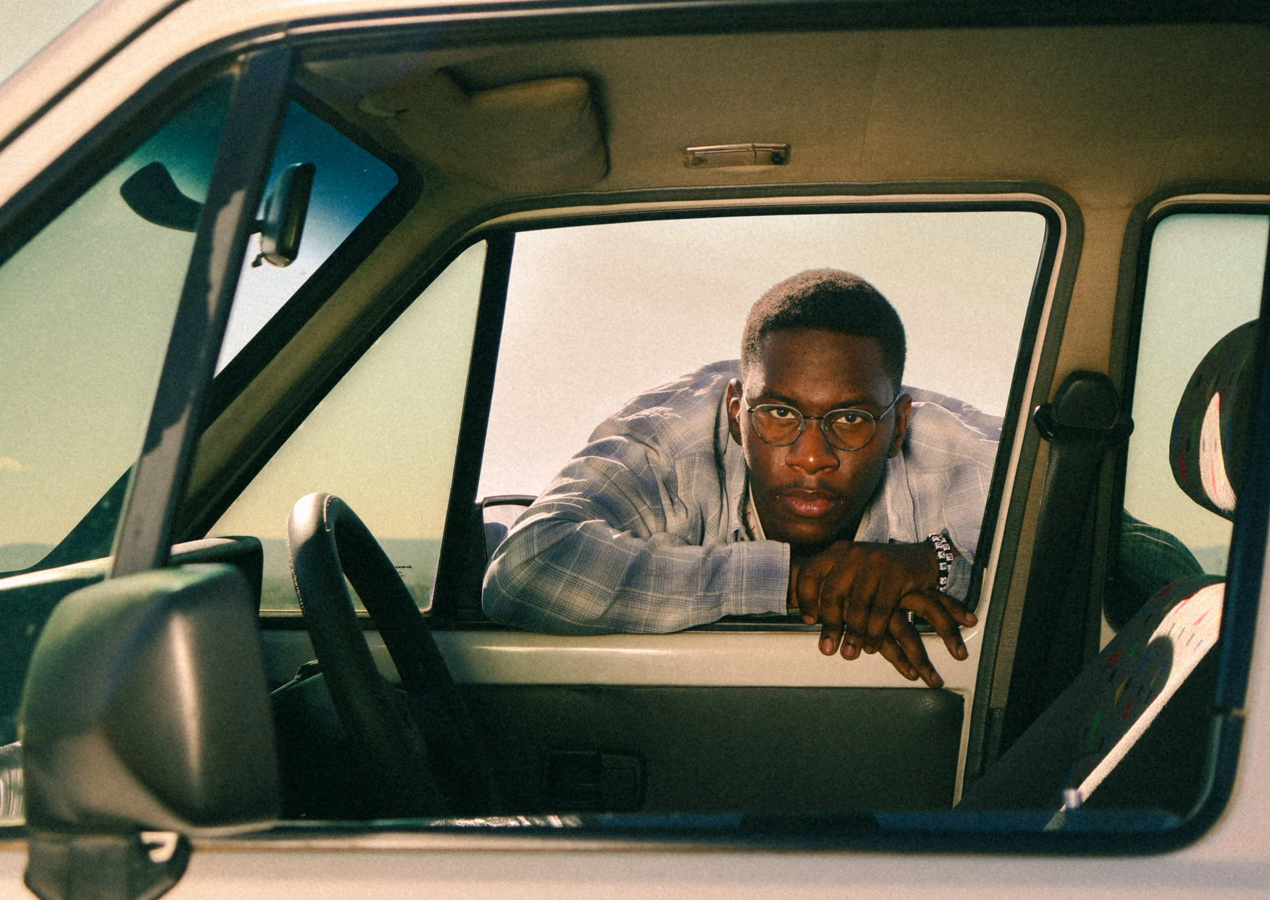 An editorial portrait photograph of Eleazar Mwakipesile leaning against a car window taken by Kim Kambinda in Windhoek, Namibia.