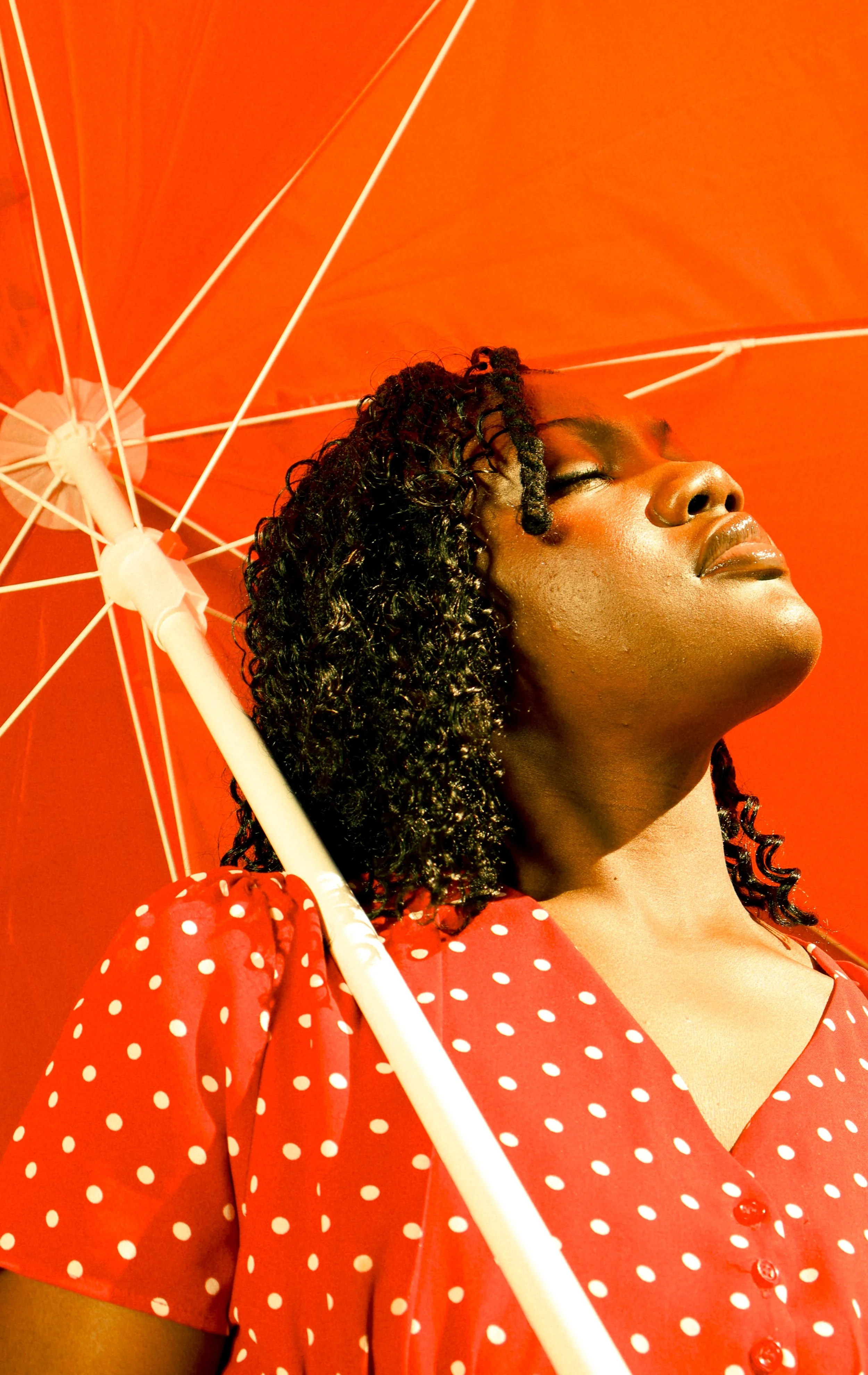 An editorial portrait photograph of Jane Simataa facing the sun while under a red umbrella taken by Kim Kambinda in Windhoek, Namibia.