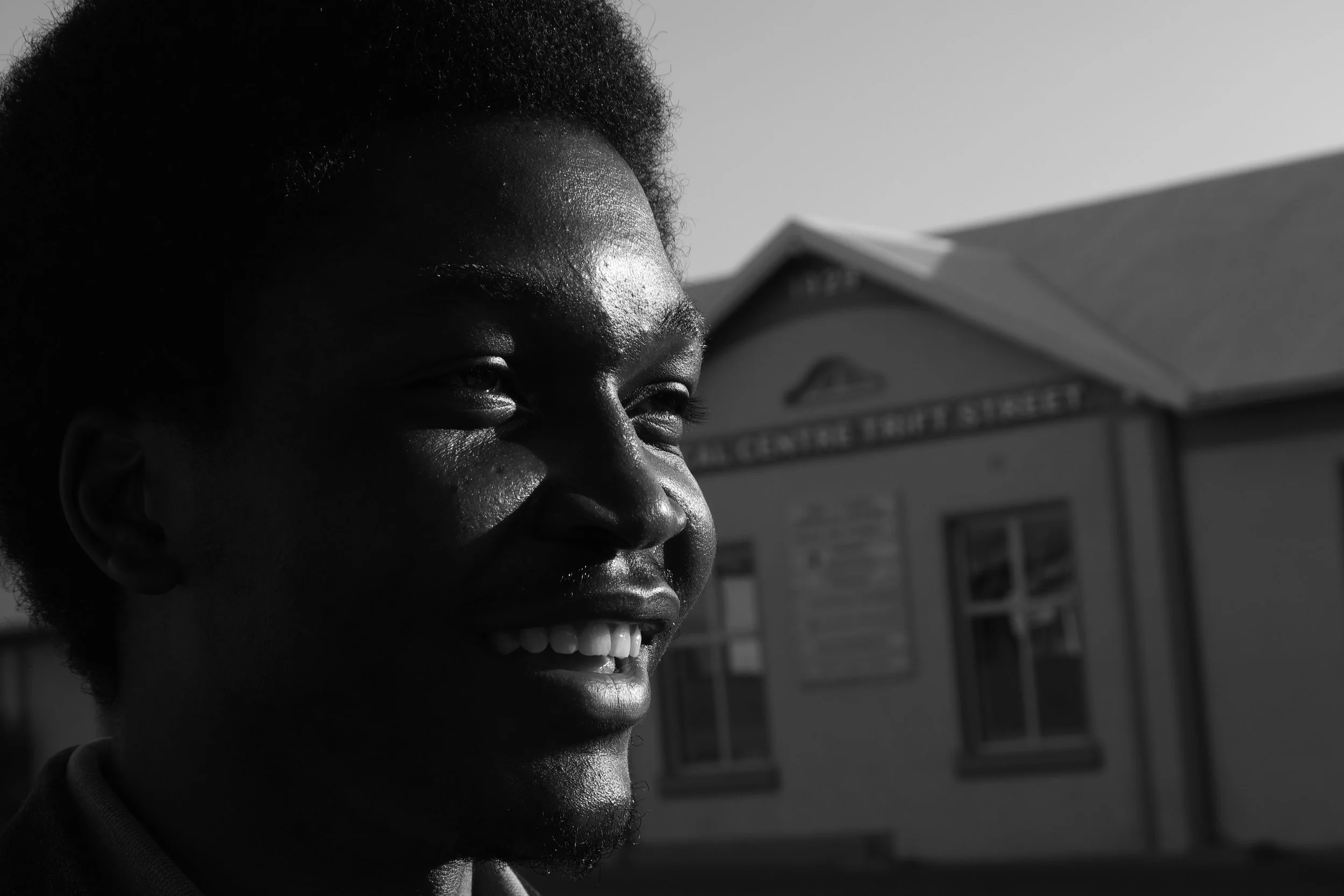 A black and white photograph of Hafeni Neliwa smiling and looking into the sun in Windhoek, Namibia taken by Kim Kambinda.