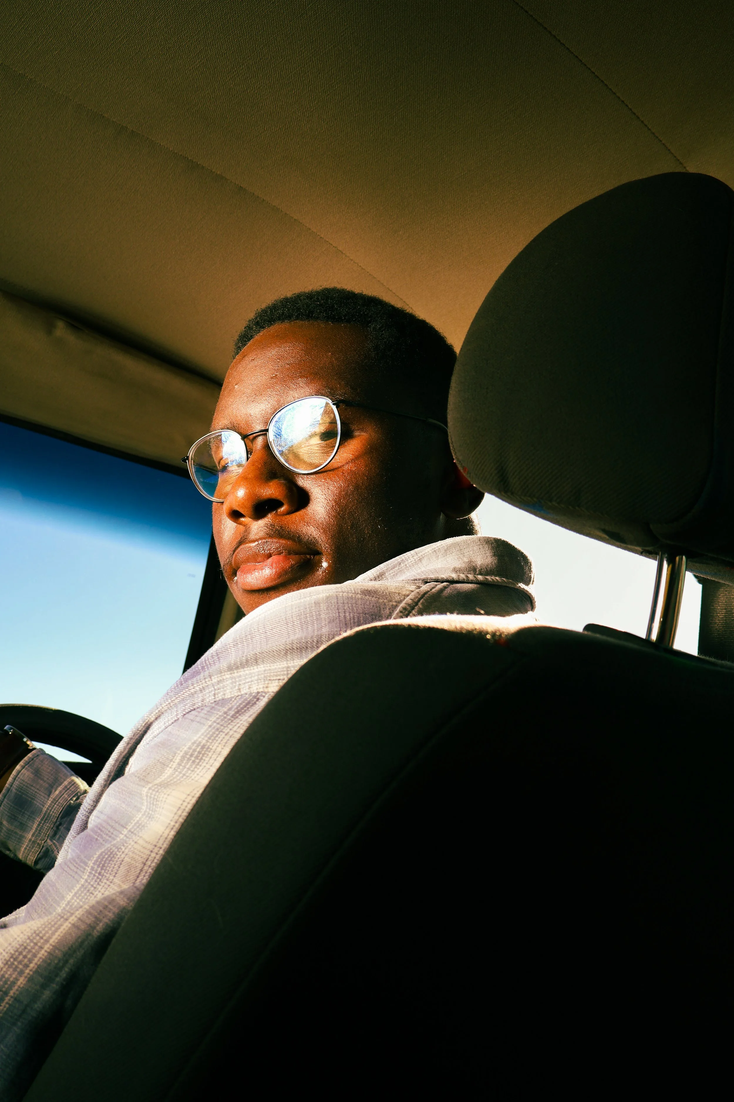 An editorial portrait photograph of Eleazar Mwakipesile sitting in his car looking down at the camera in the backseat taken by Kim Kambinda in Windhoek, Namibia.