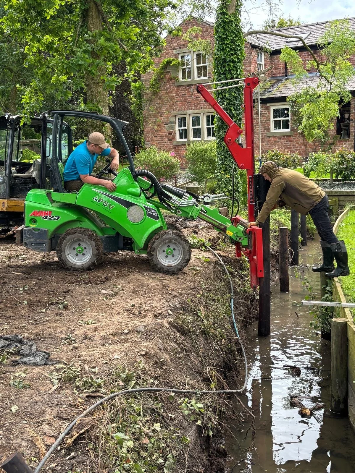 Avant compact loader with post knocker driving fence posts on site