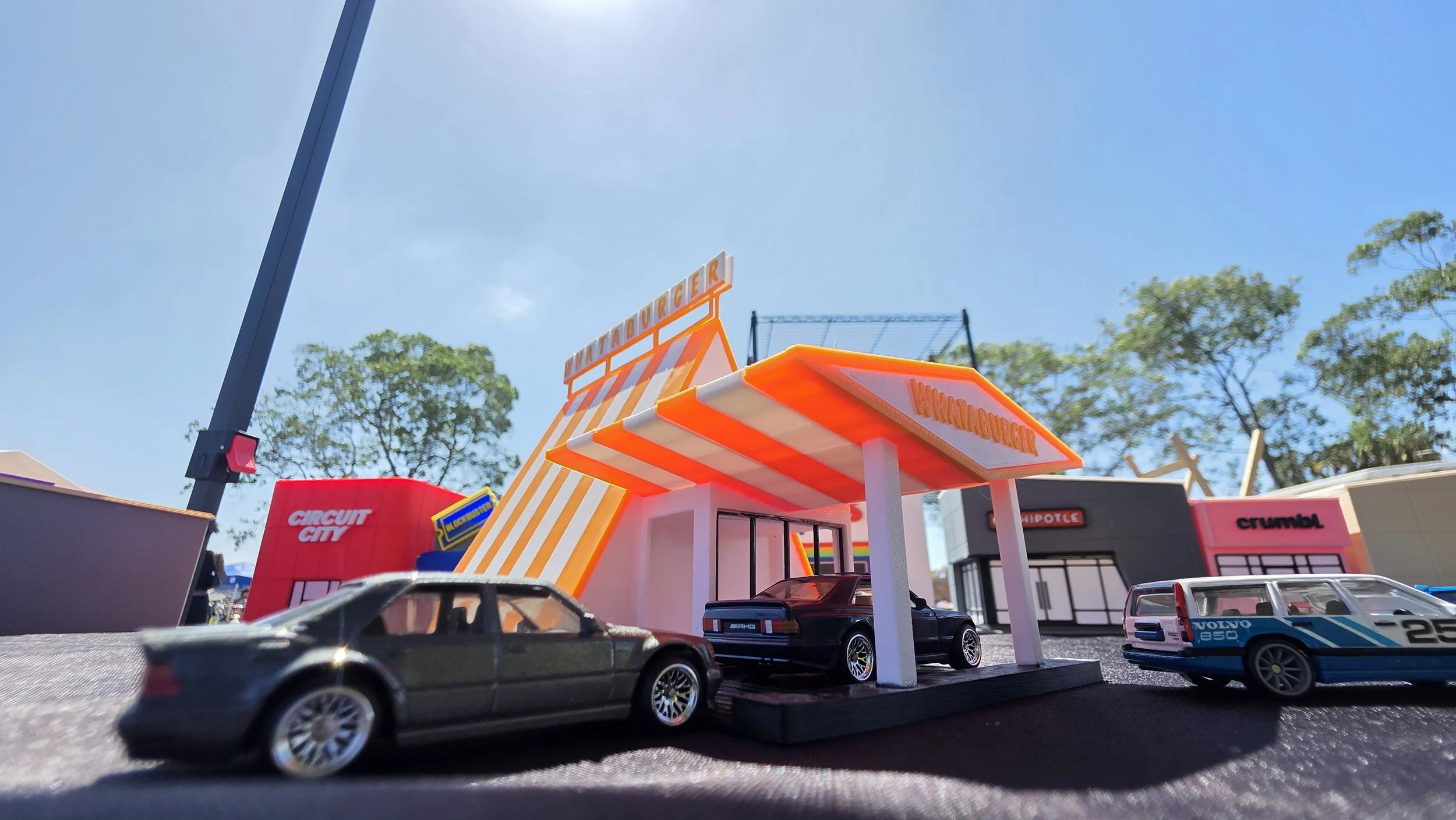 Miniature model of a fast food restaurant with bright orange and white striped awning, cars parked in front, and signage for a burger joint.