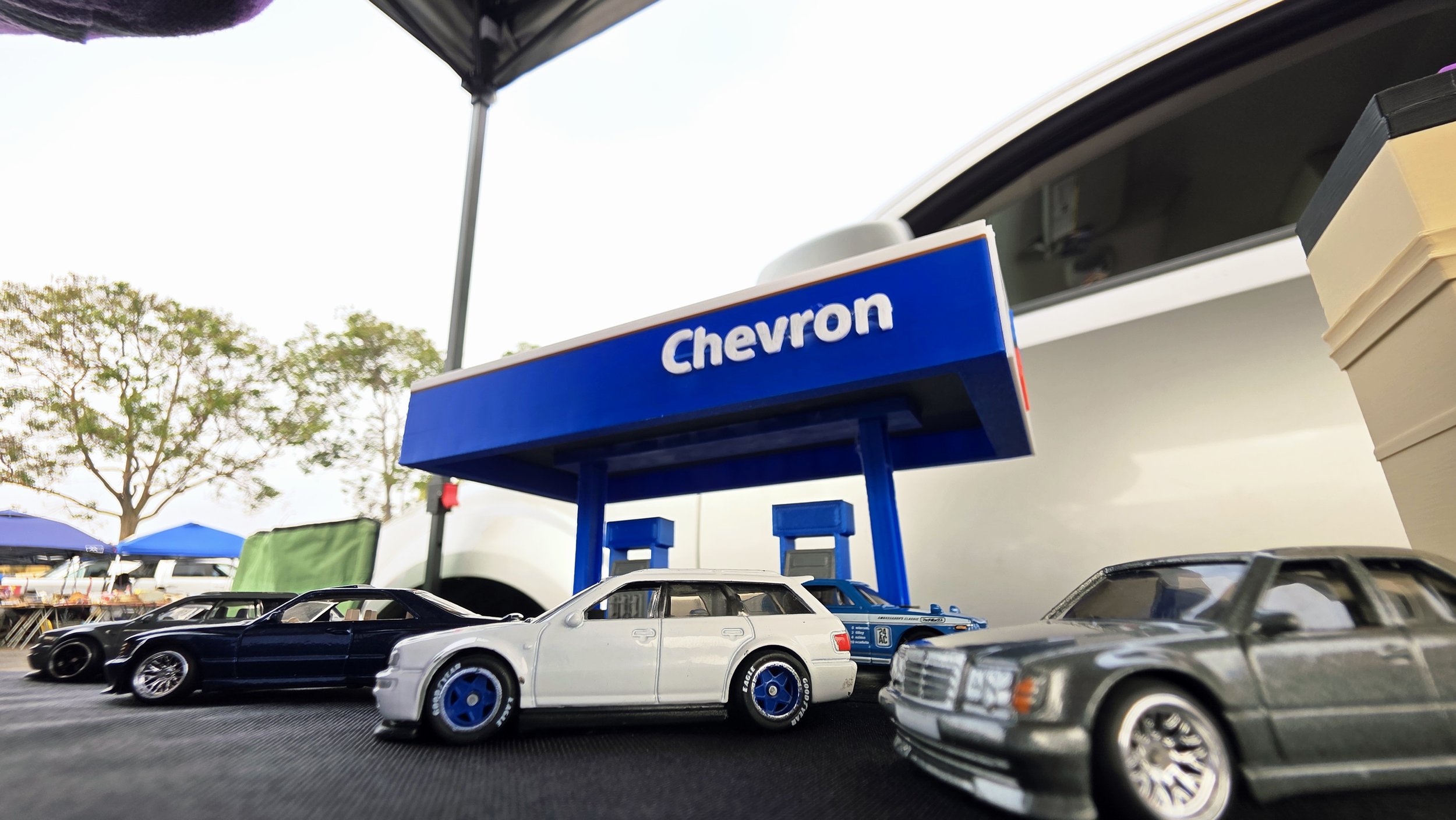 Close-up of toy cars on a display table with a Chevron gas station sign in the background.