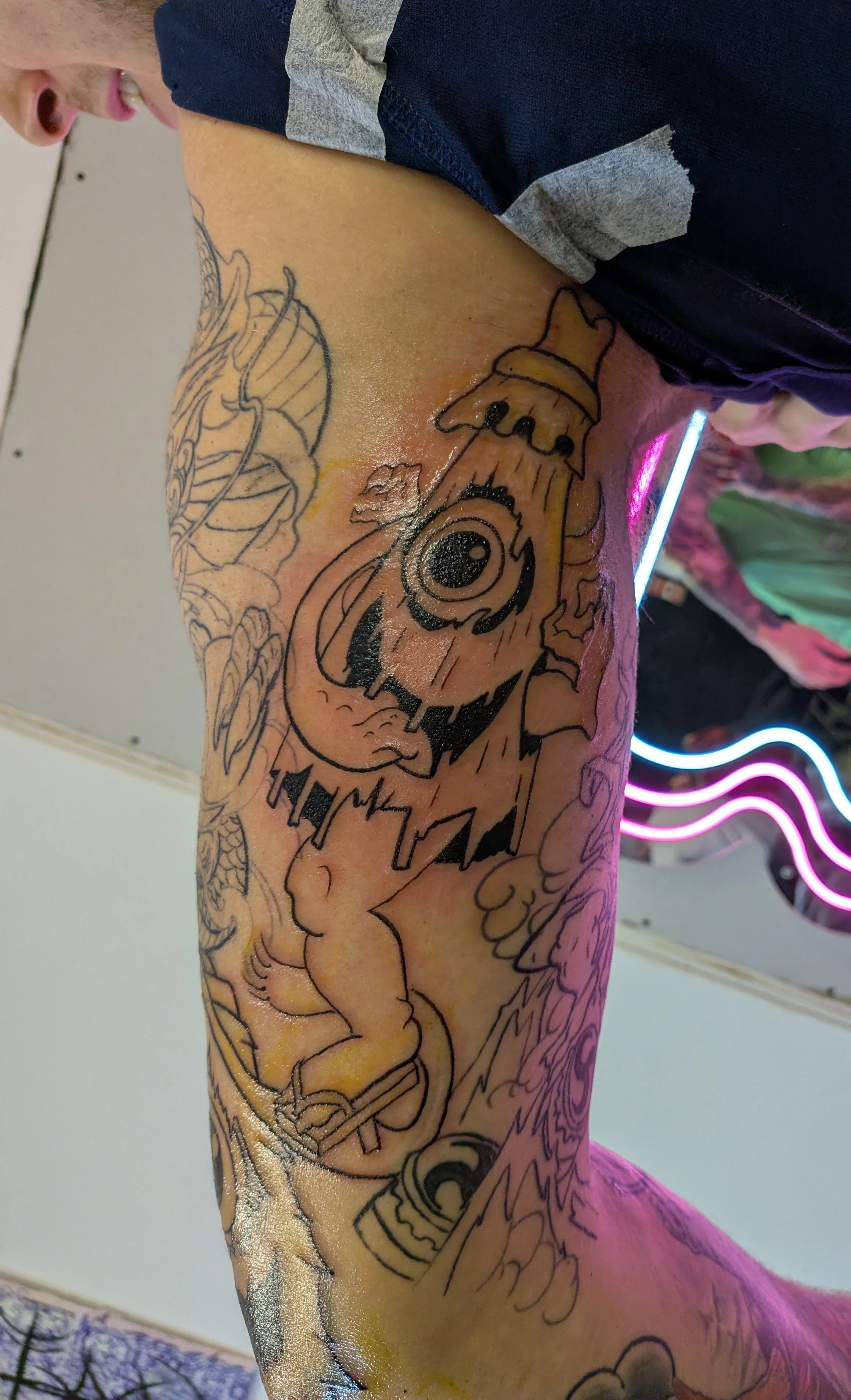 Close-up of a person’s arm with a detailed cartoon character tattoo, wearing a dark sleeve and gray wristband.