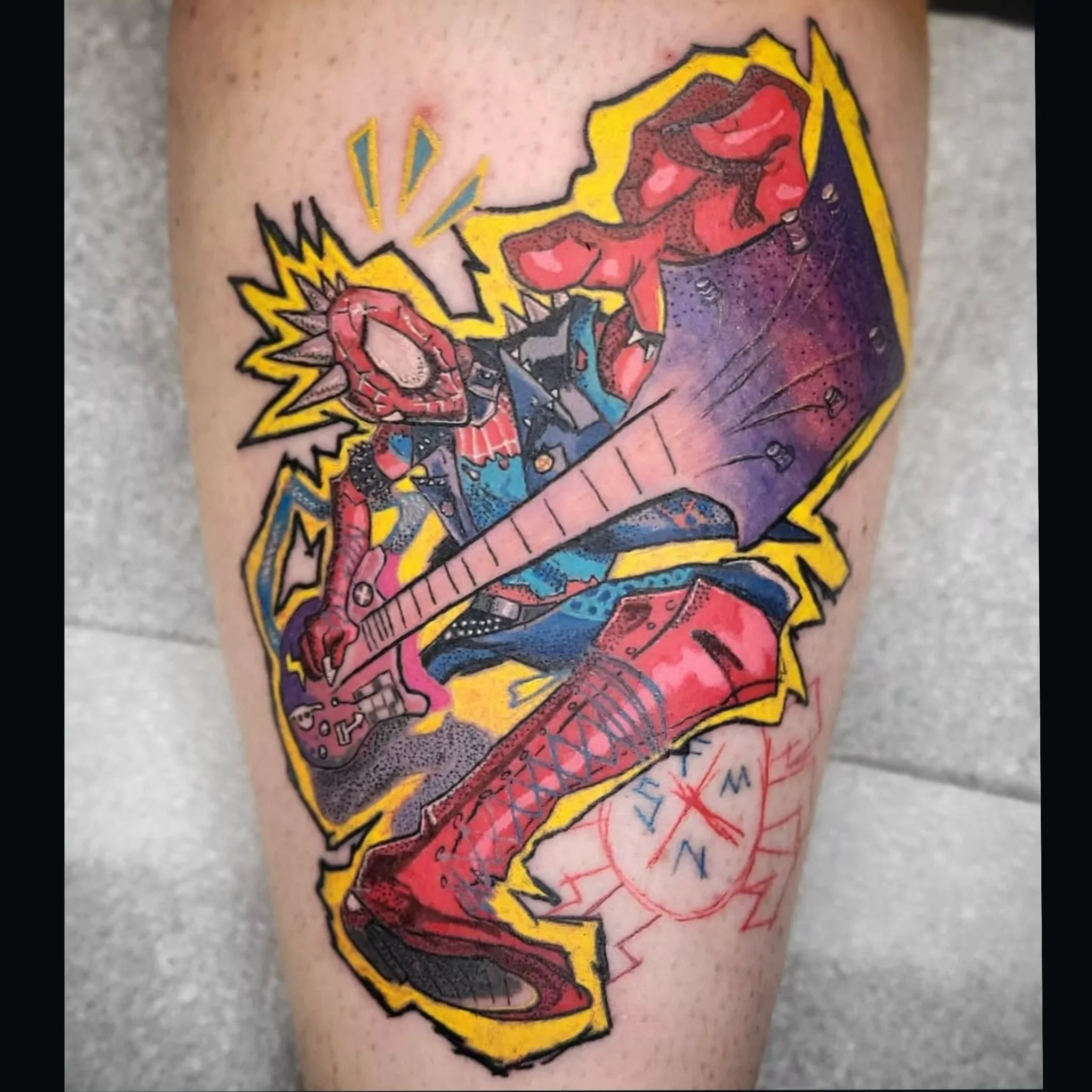 Colorful comic-book style tattoo featuring an electric guitar, punk rock imagery, and yellow lightning bolts on a leg