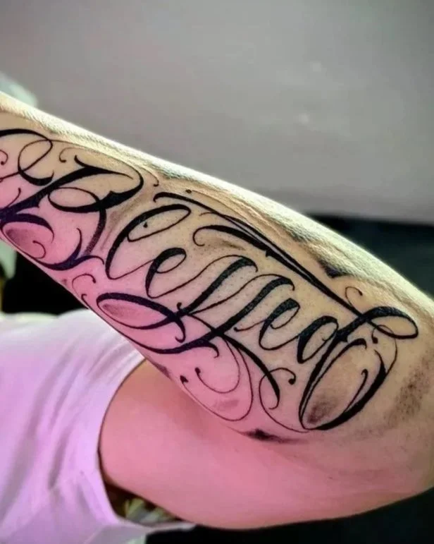 Close-up of ornate black calligraphy tattoo reading “Family” on a person’s upper arm.