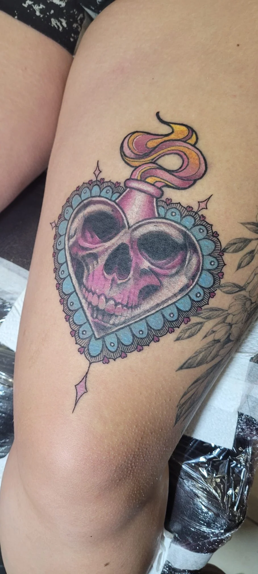 Colorful tattoo of a skull-shaped heart with a snake emerging from a pink anatomical heart, surrounded by blue floral details.