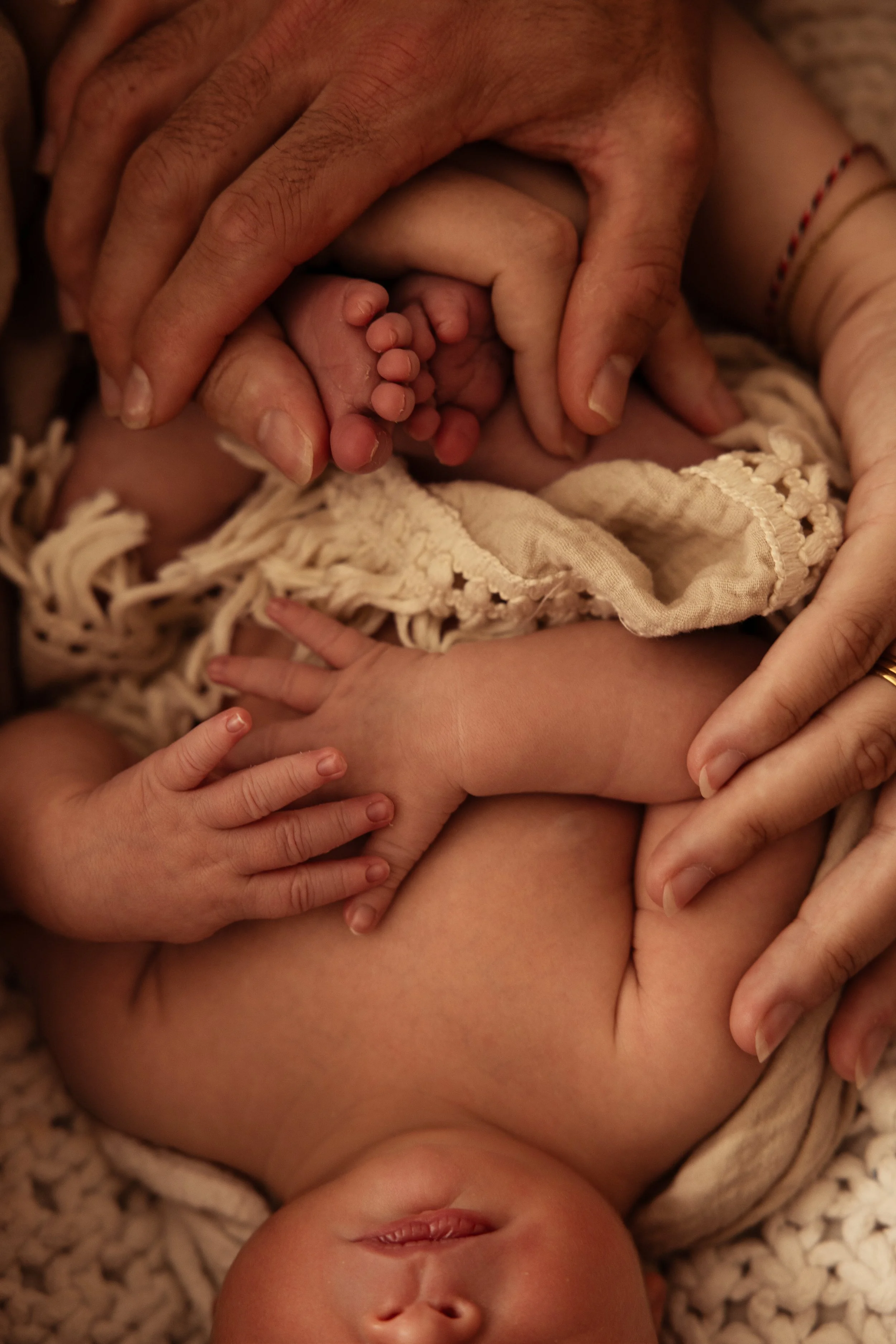 Nouveau-né entouré de ses parents dans un moment de douceur et de bienveillance, illustrant le lien parent-bébé et la réflexologie bébé émotionnelle, avec une attention portée aux mains et aux pieds.
