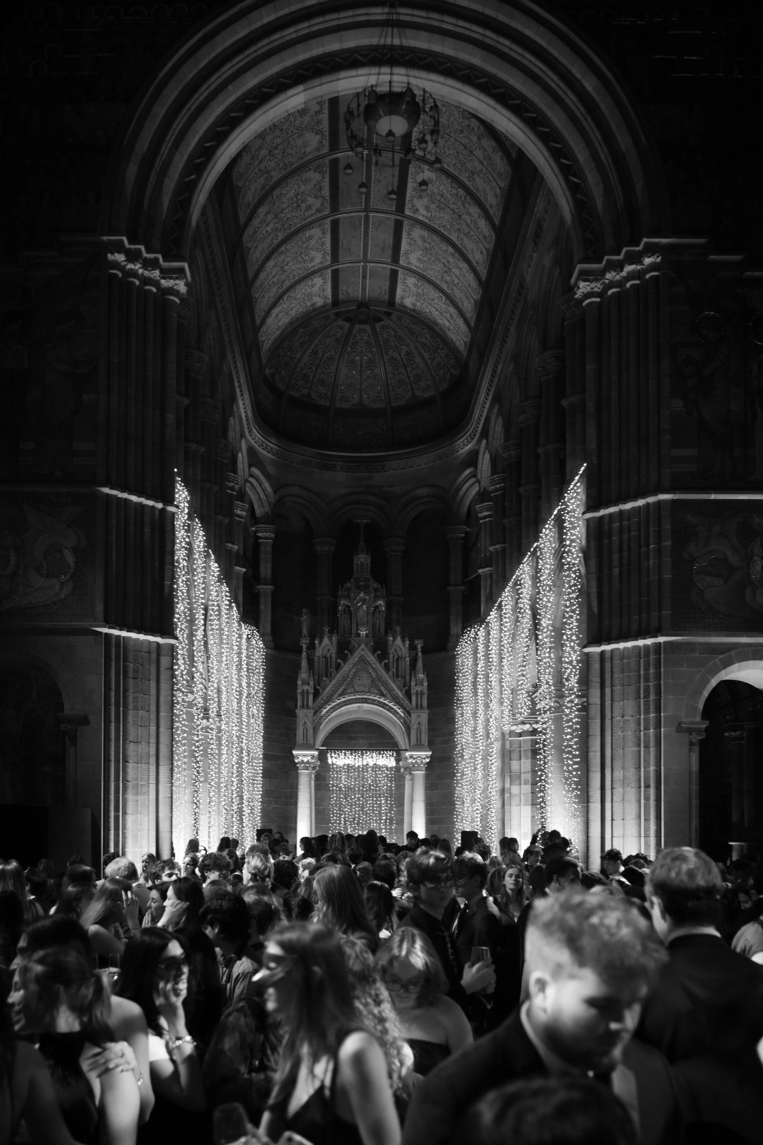 Crowd of people gathered inside a grand, ornate cathedral decorated with Christmas lights.