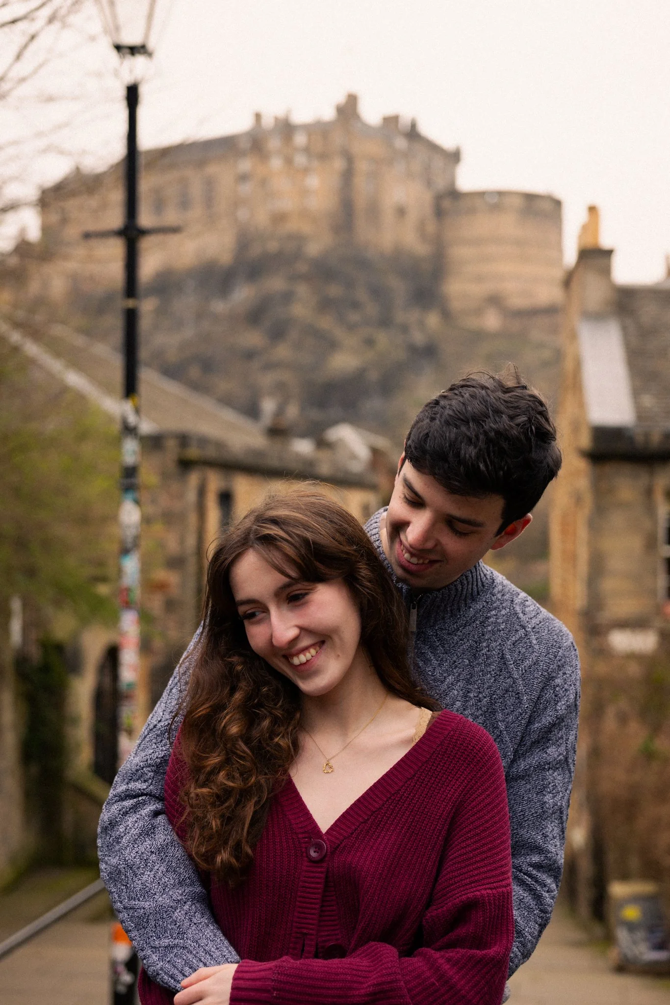A young couple embracing on a bridge with a castle on a hill in the background.