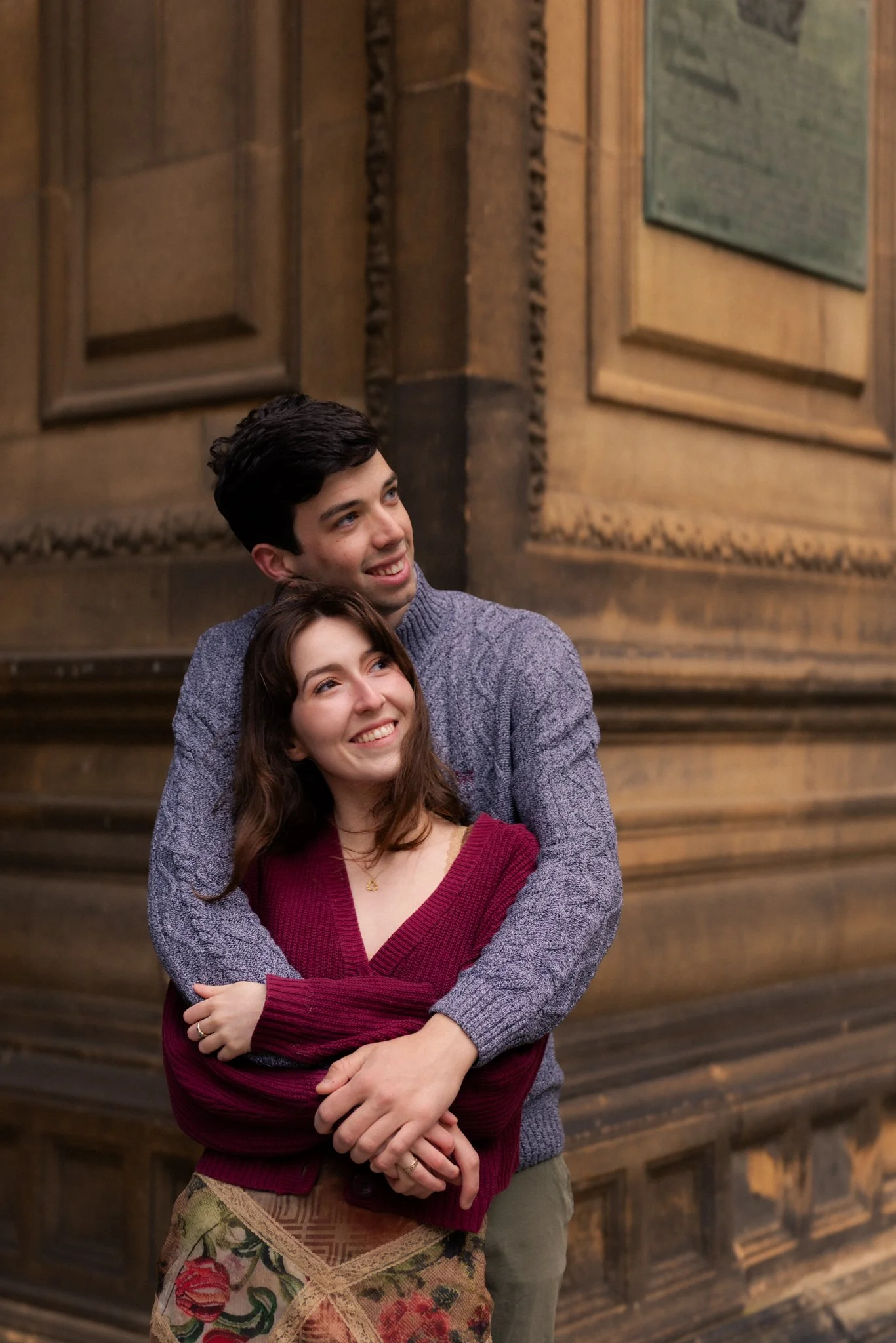 A young couple hugging each other and smiling inside a building with wooden paneled walls.