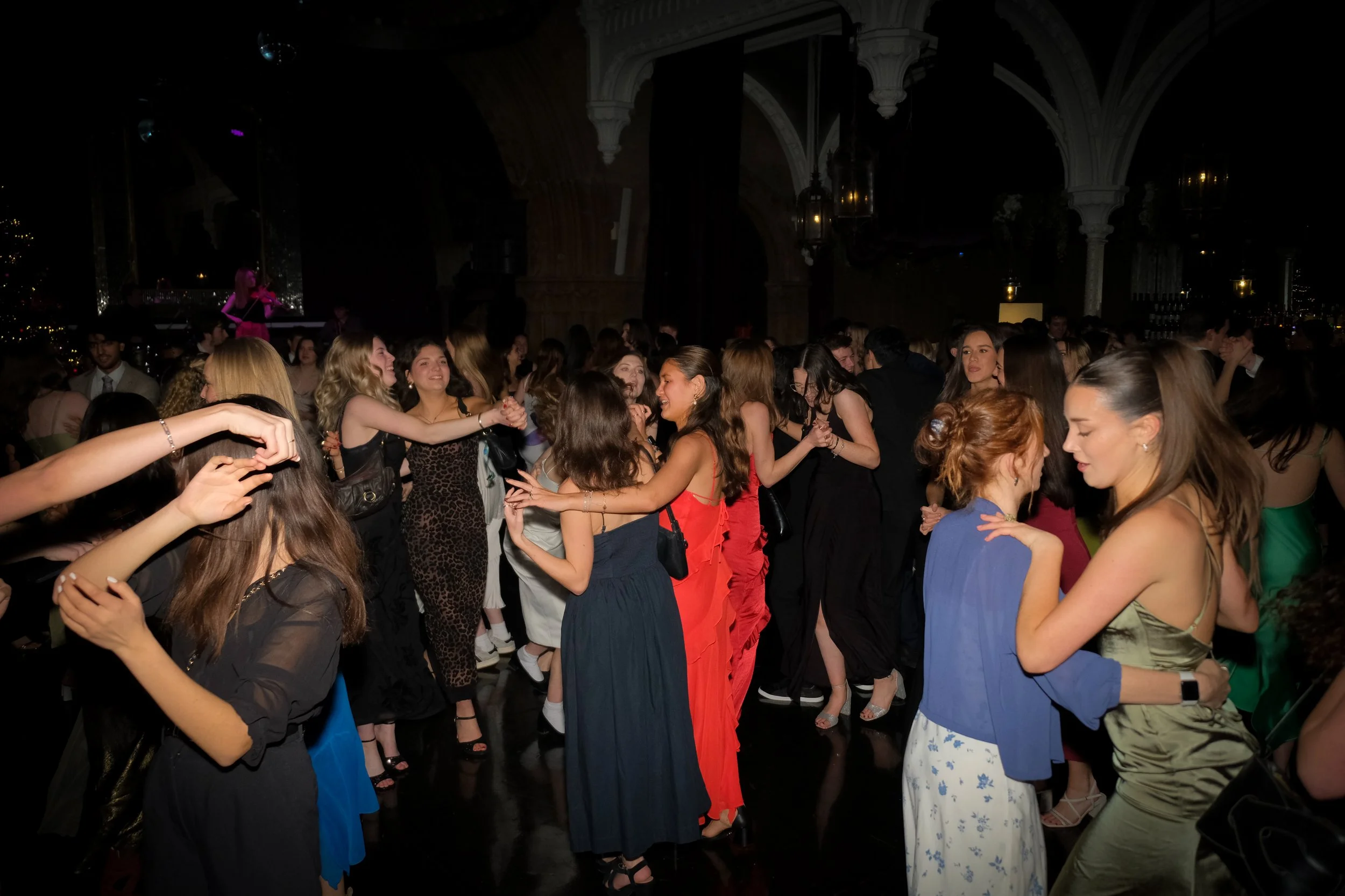 People dancing at a party or celebration in an elegant venue with arched ceilings and lantern lights.