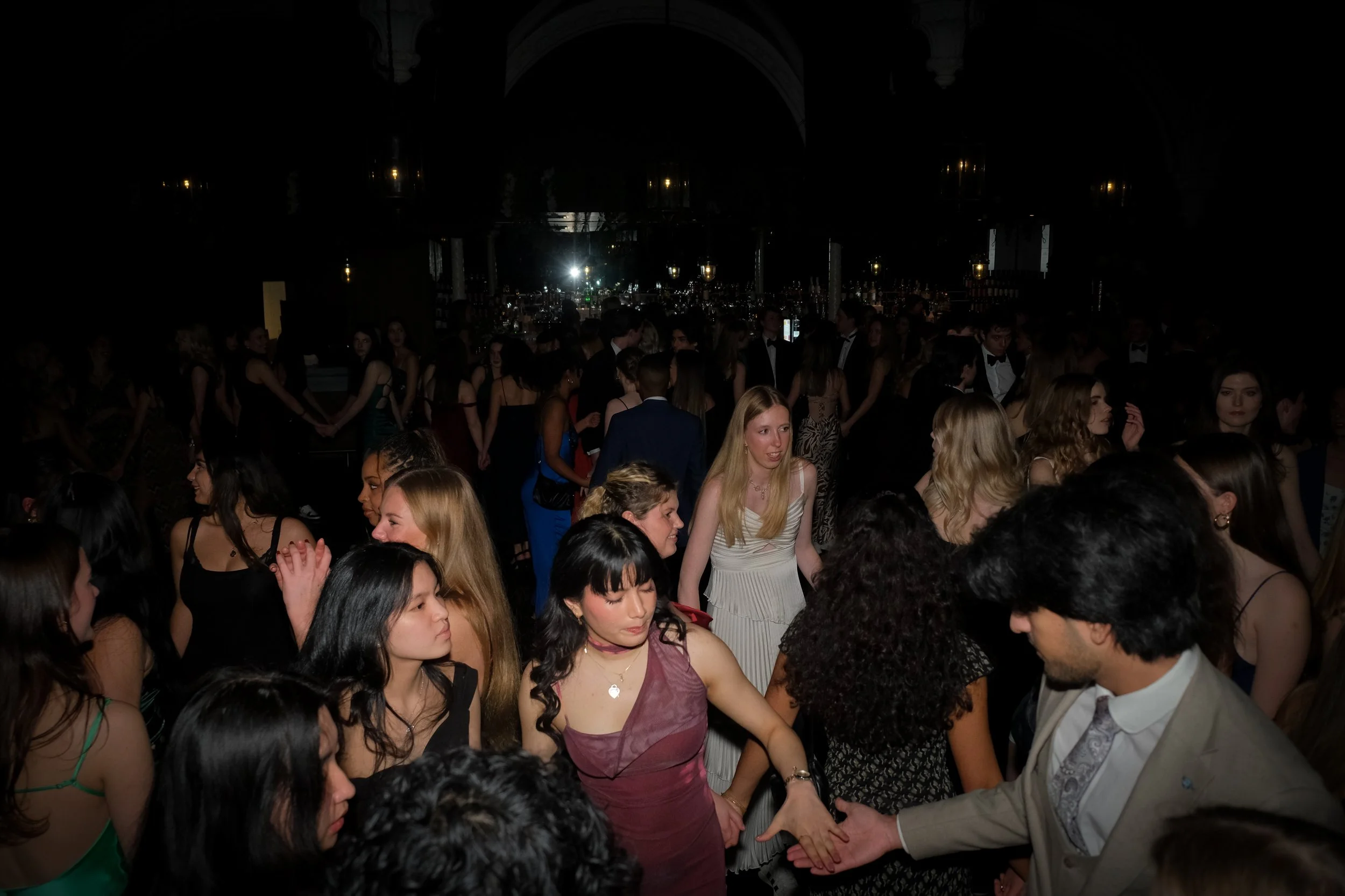 Young people dancing at a formal event with a dark background, some holding hands and others in conversation.