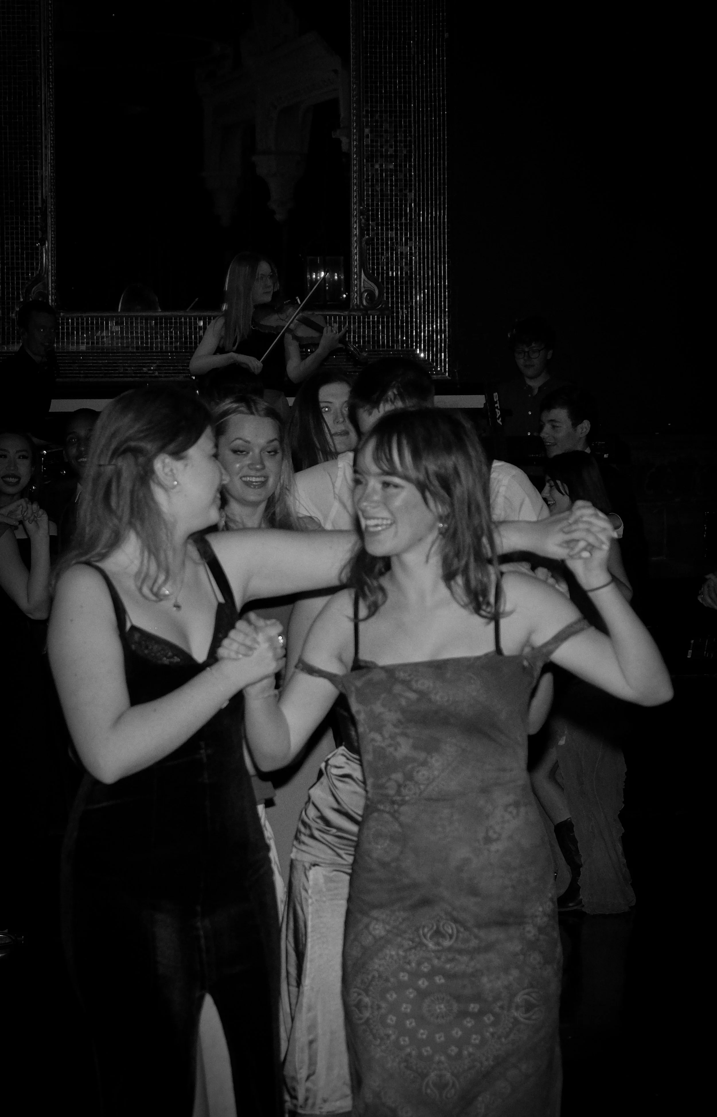 Two women dancing closely and smiling at each other while holding hands in a lively social gathering.