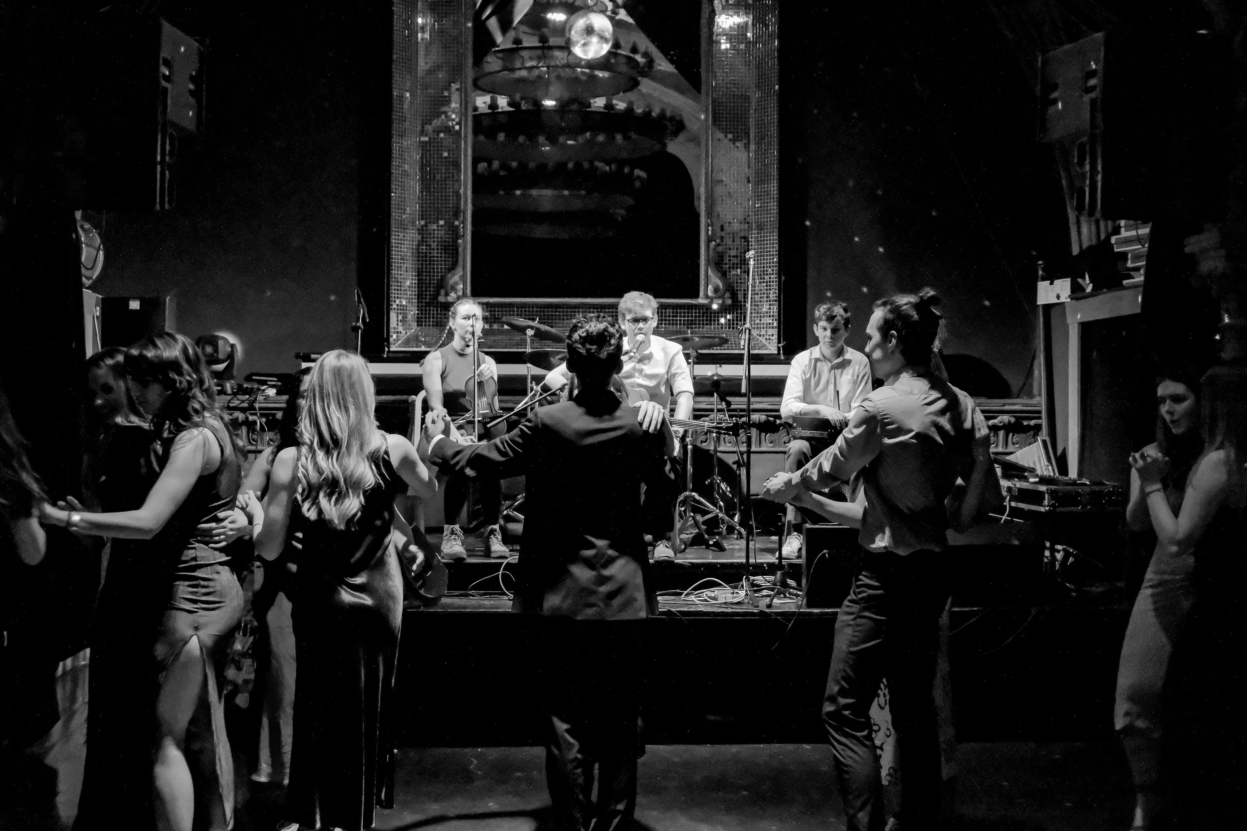 Black and white photo of a live music concert with a band performing on stage and people dancing in front.