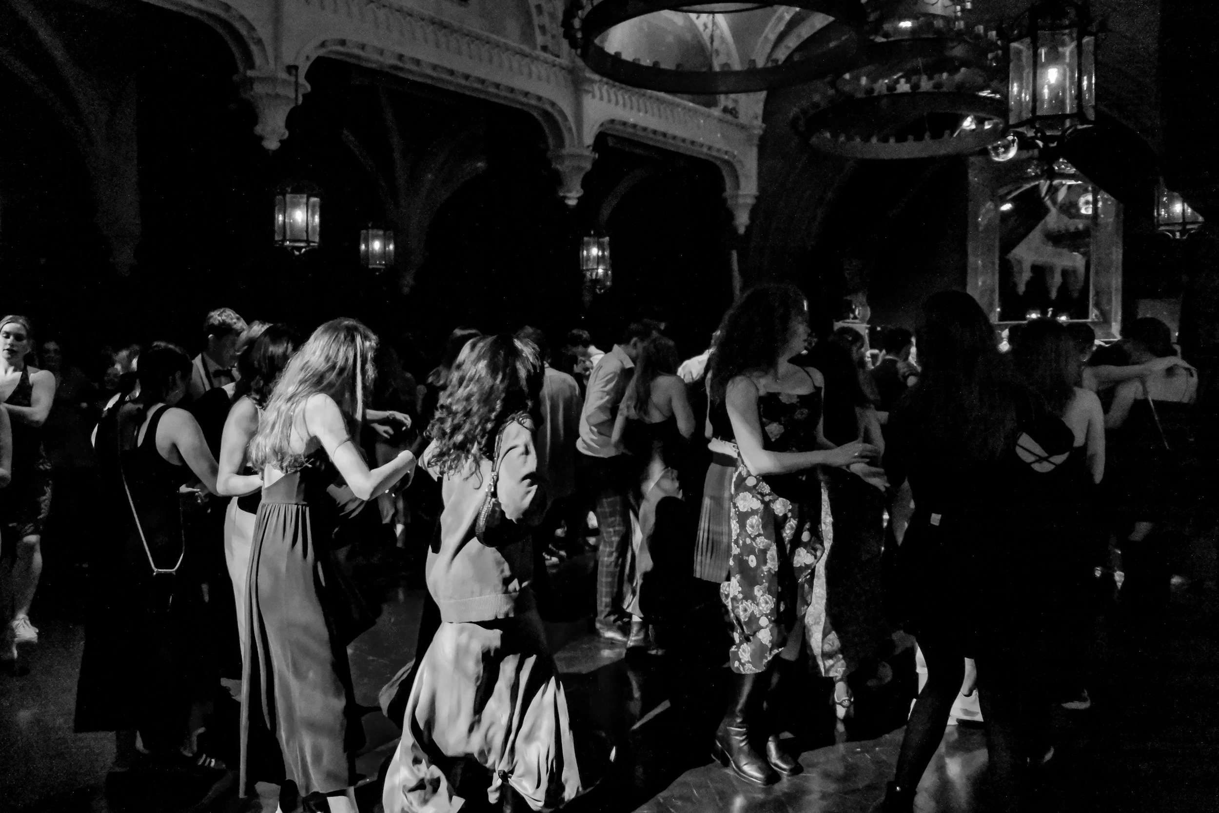 Group of people dancing at a dark, ornate venue with high arched ceilings and hanging lantern-style lights.