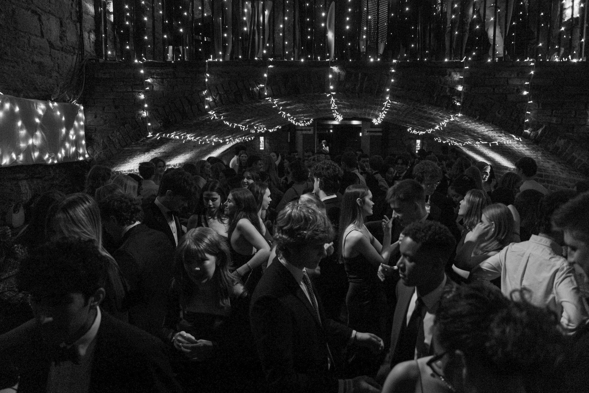 People dancing at a party under string lights in a brick-walled venue.