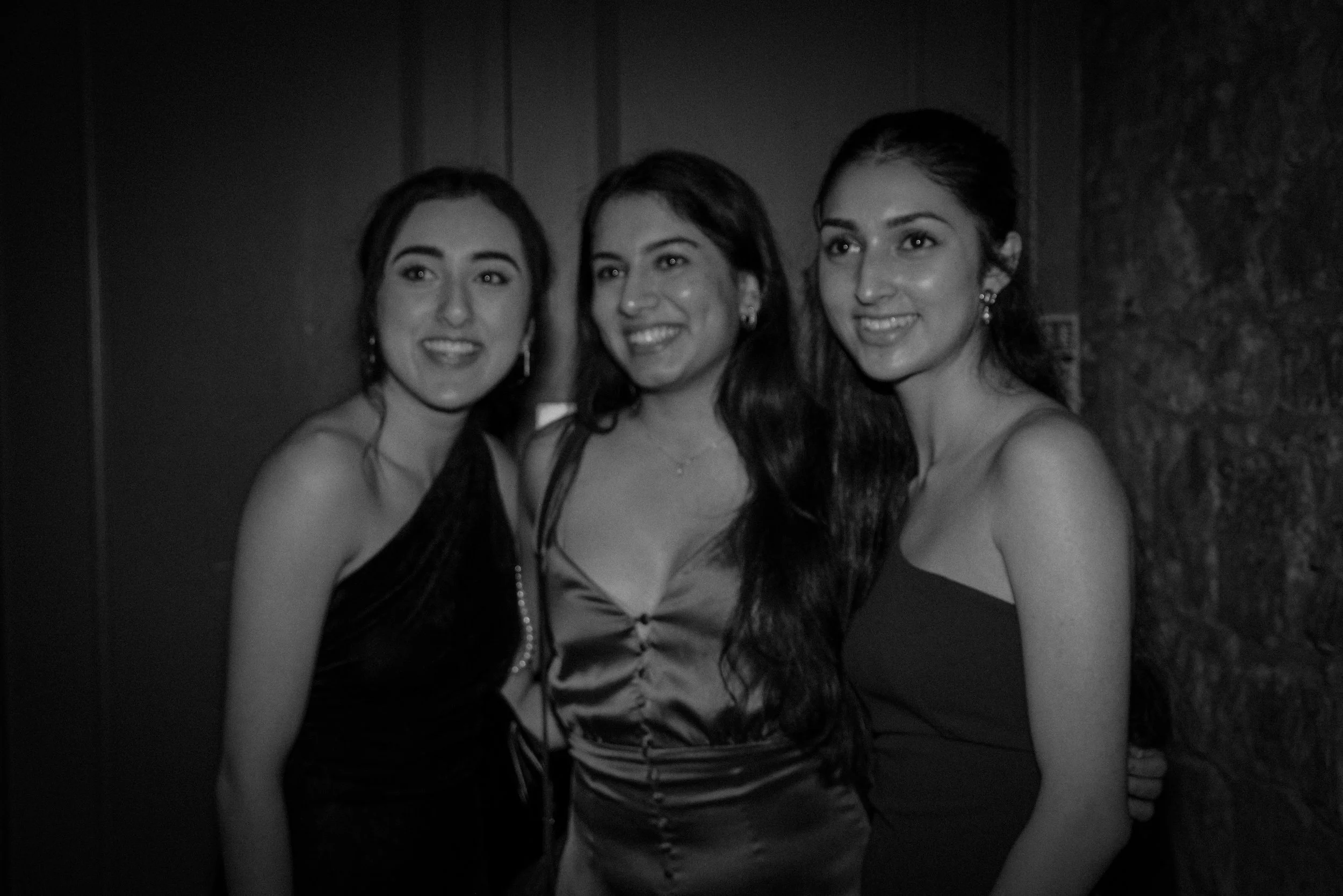 Three women in evening dresses smiling, posing together at a social event.
