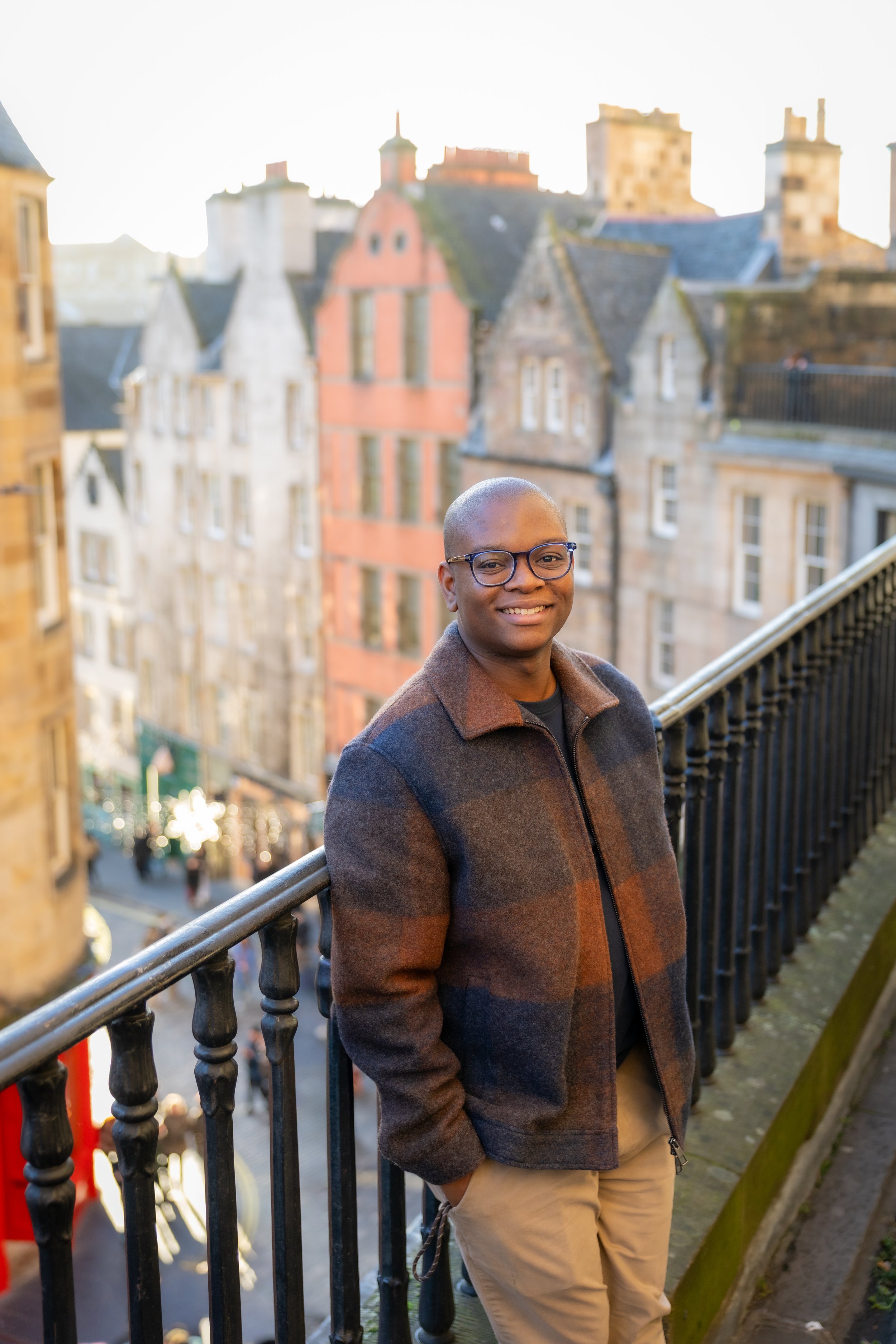 Man standing on a balcony overlooking a street with historic buildings in the background, smiling at the camera.
