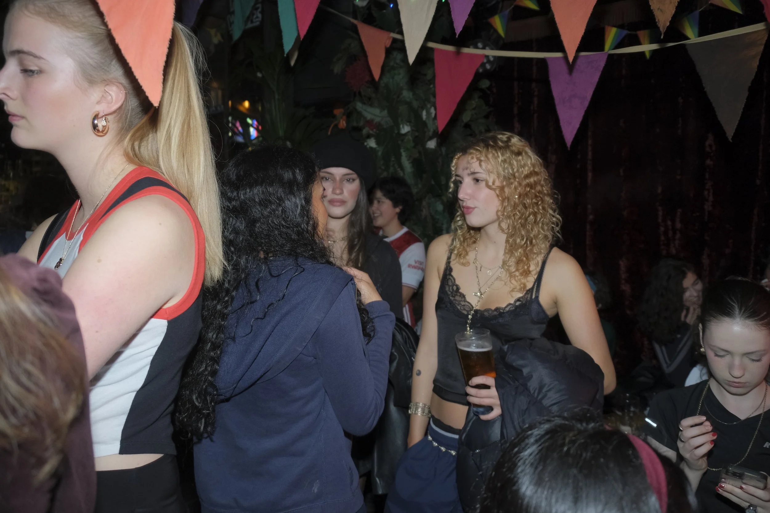 Group of people socializing at a party or nightclub with colorful pennant banners hanging from the ceiling.