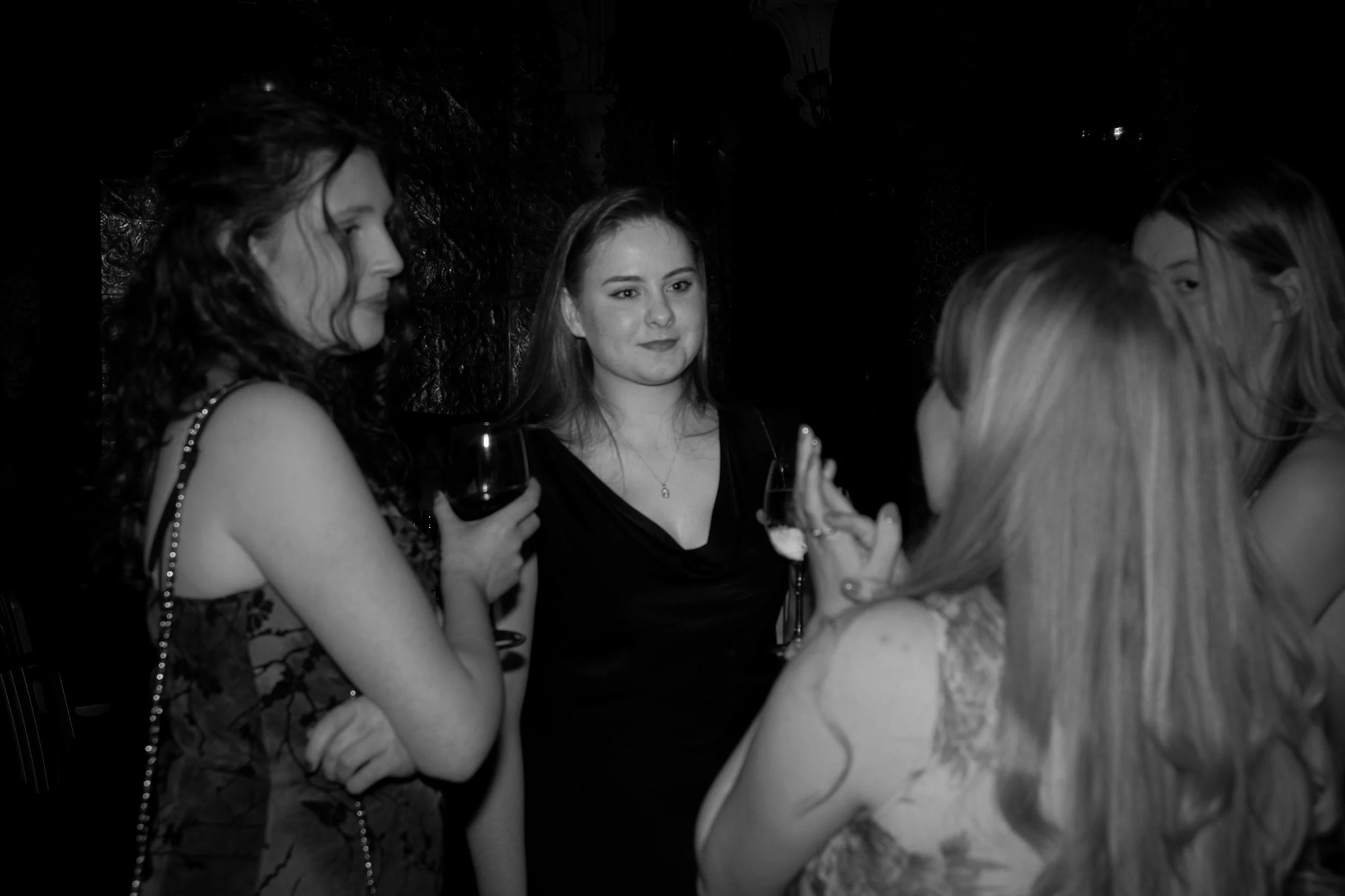 Group of women socializing at a party, holding glasses of wine, engaged in conversation.