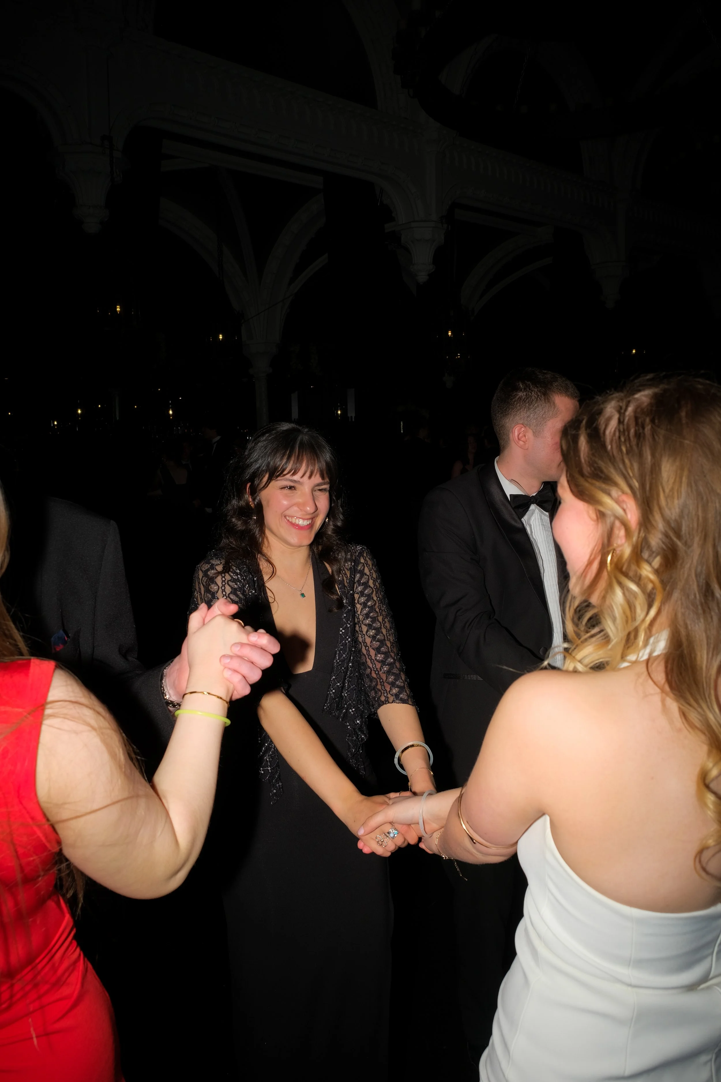 People dancing at a formal event, smiling, and holding hands, dressed in elegant evening attire.