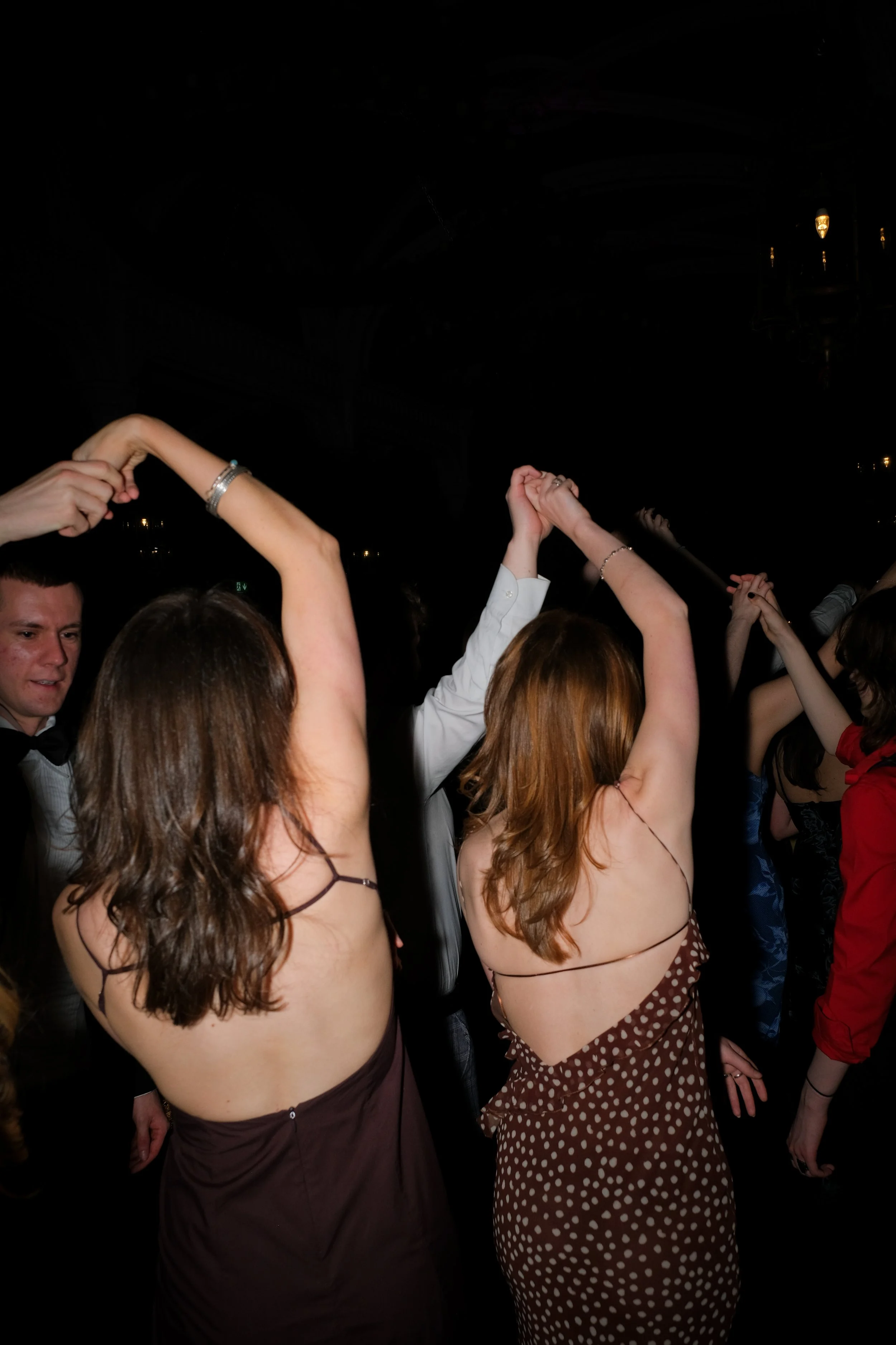 People dancing at a night event with raised arms, some wearing formal attire.