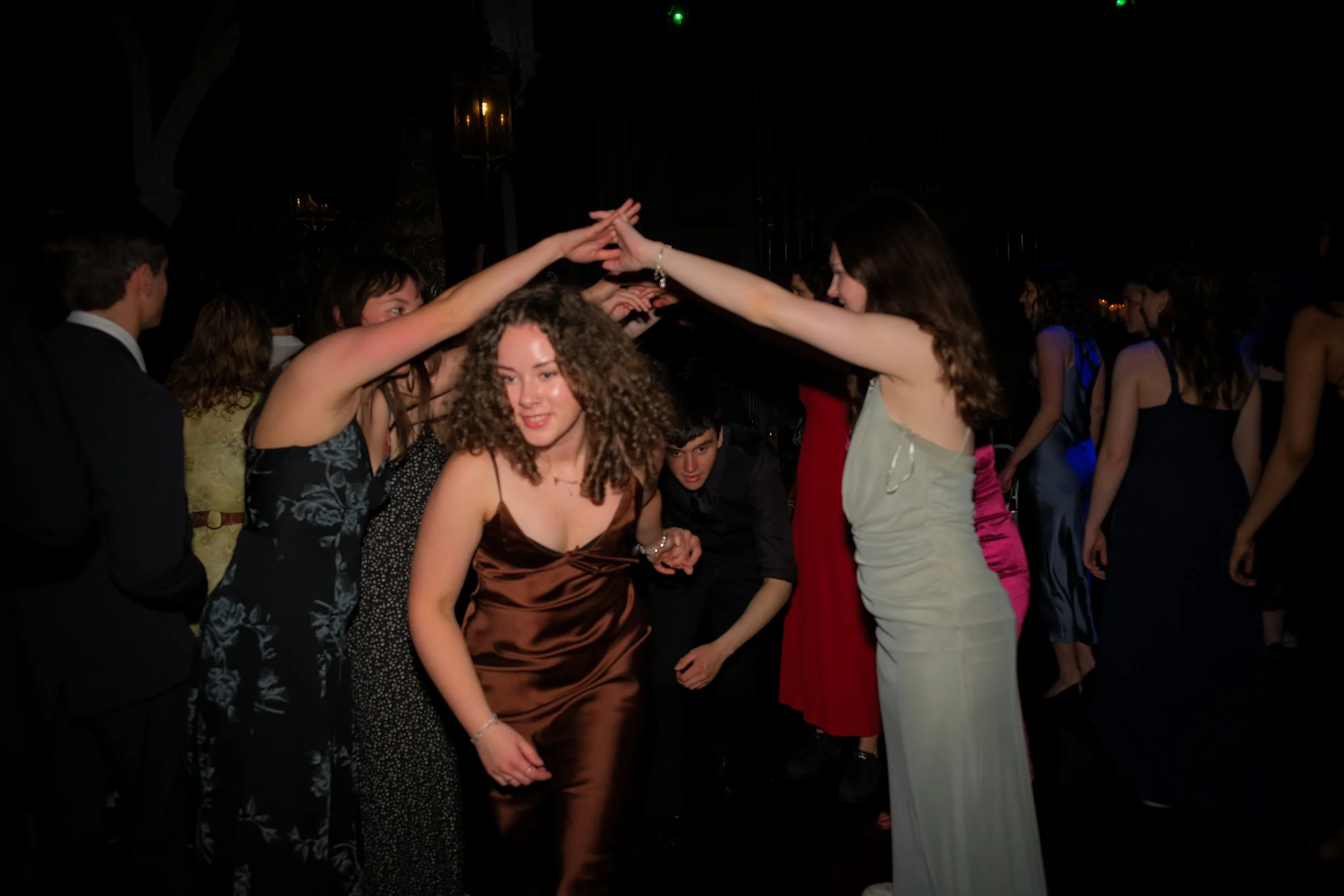 People dancing in formal attire at a social event, forming a tunnel with their arms.