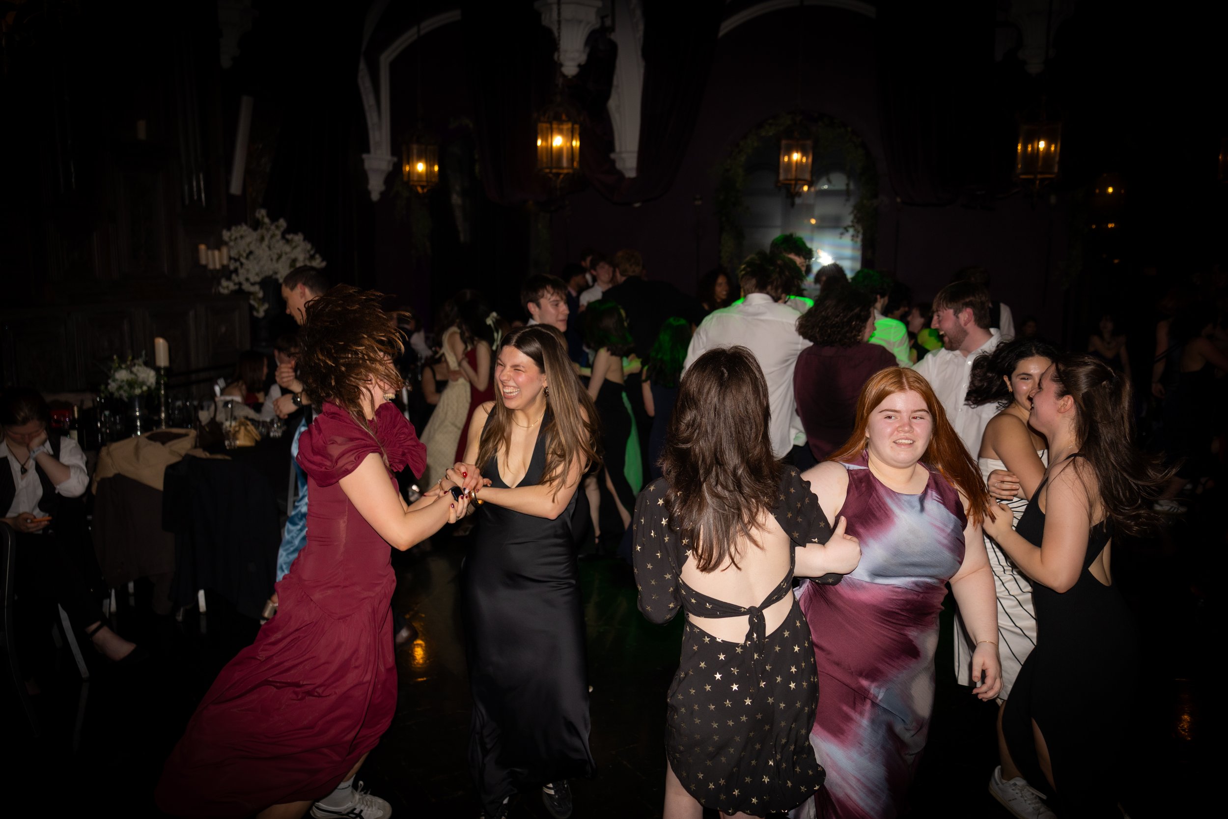 People dancing and socializing at a lively indoor party or dance event with dim lighting and elegant decor.